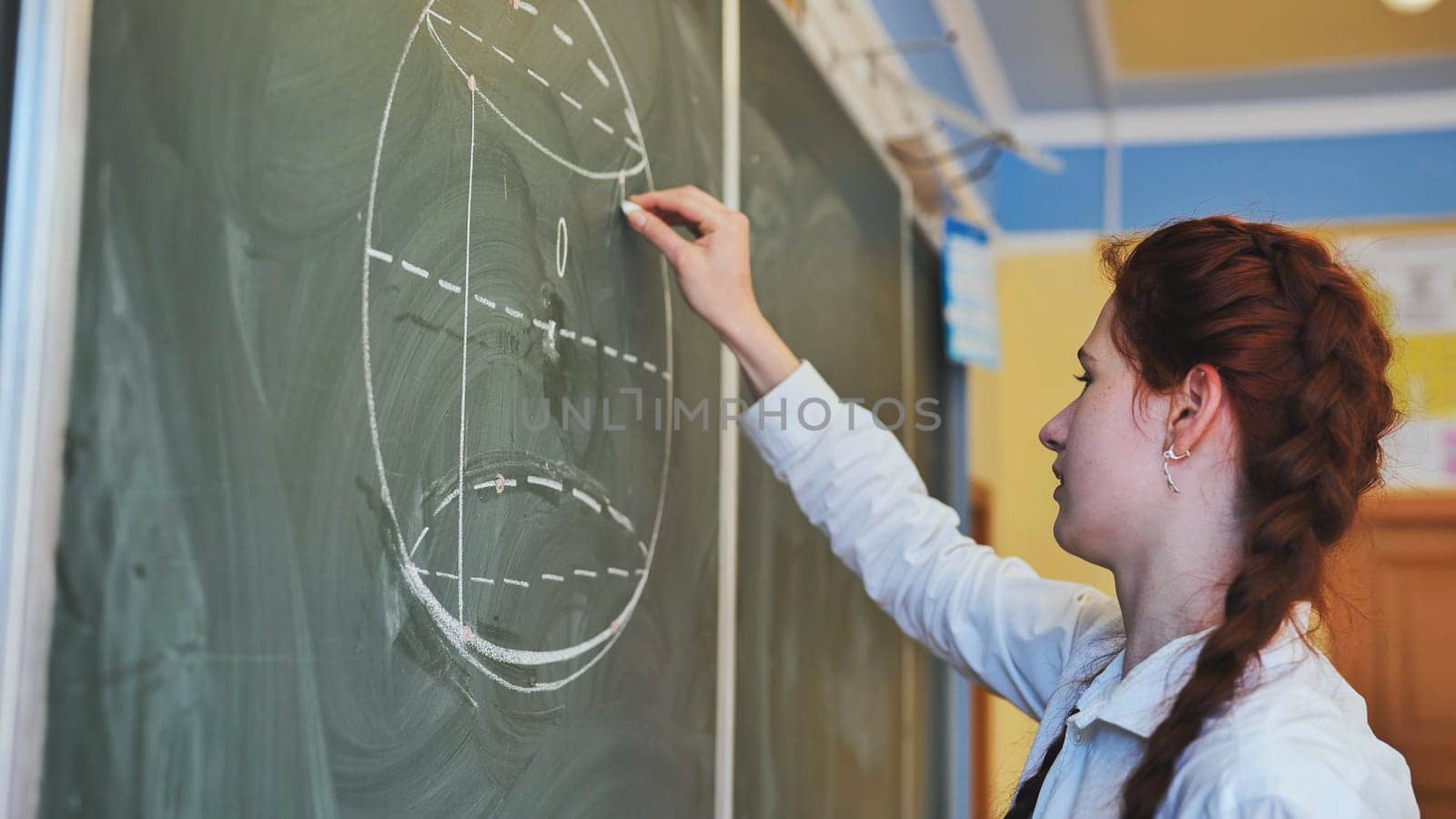 A red-haired schoolgirl draws geometric shapes on the board