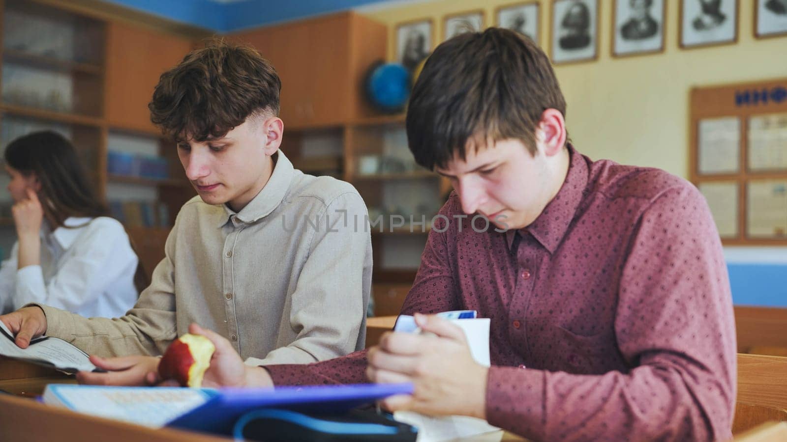 Schoolboys at a desk during class. The boy eats an apple