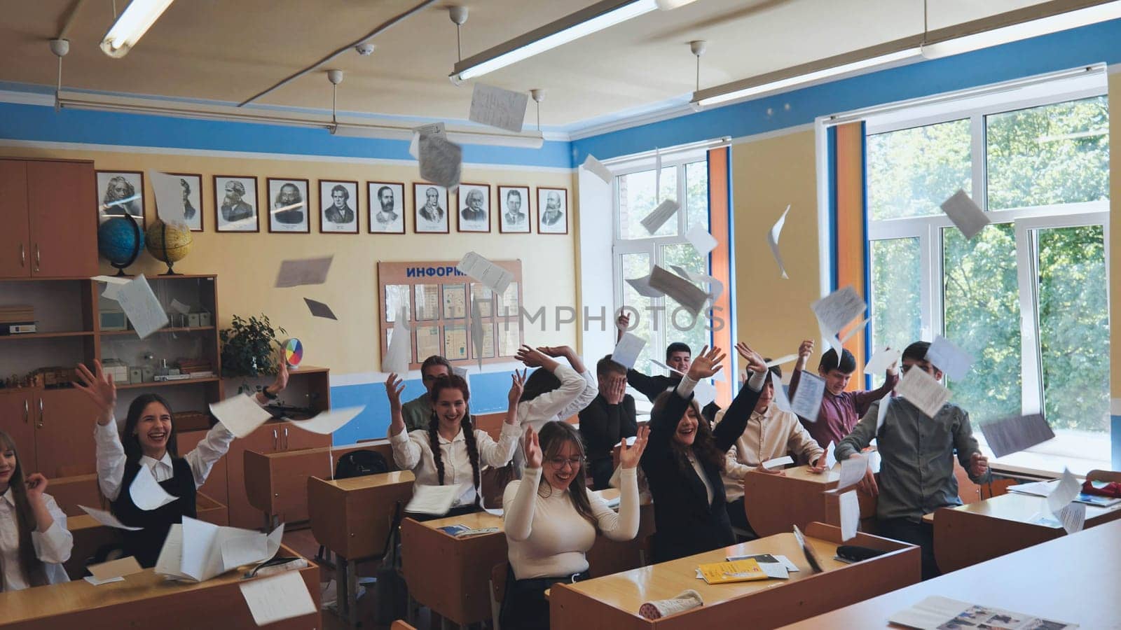 Berezovka, Belarus - May 15, 2023: Students toss notebooks and books up in their classroom. by DovidPro