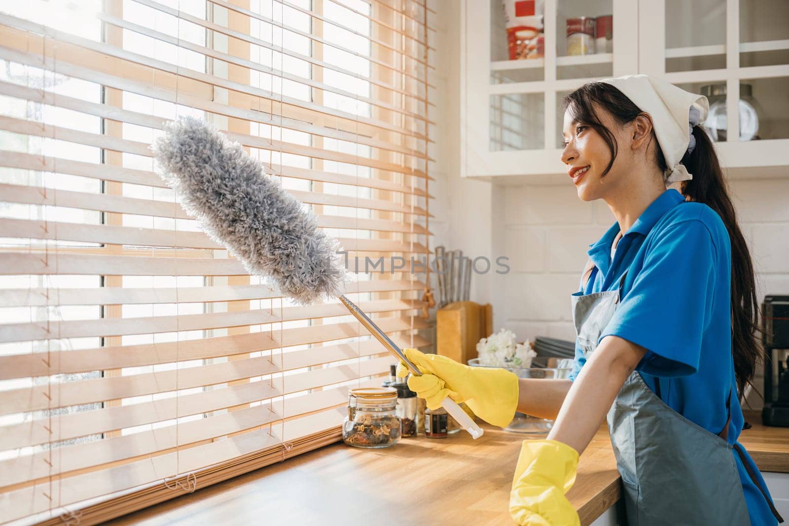 Woman enjoys routine housework cleaning dirty window blinds. Standing with duster and feather whisk ensuring hygiene. Modern cleaning for a clean home is portrayed. whisk