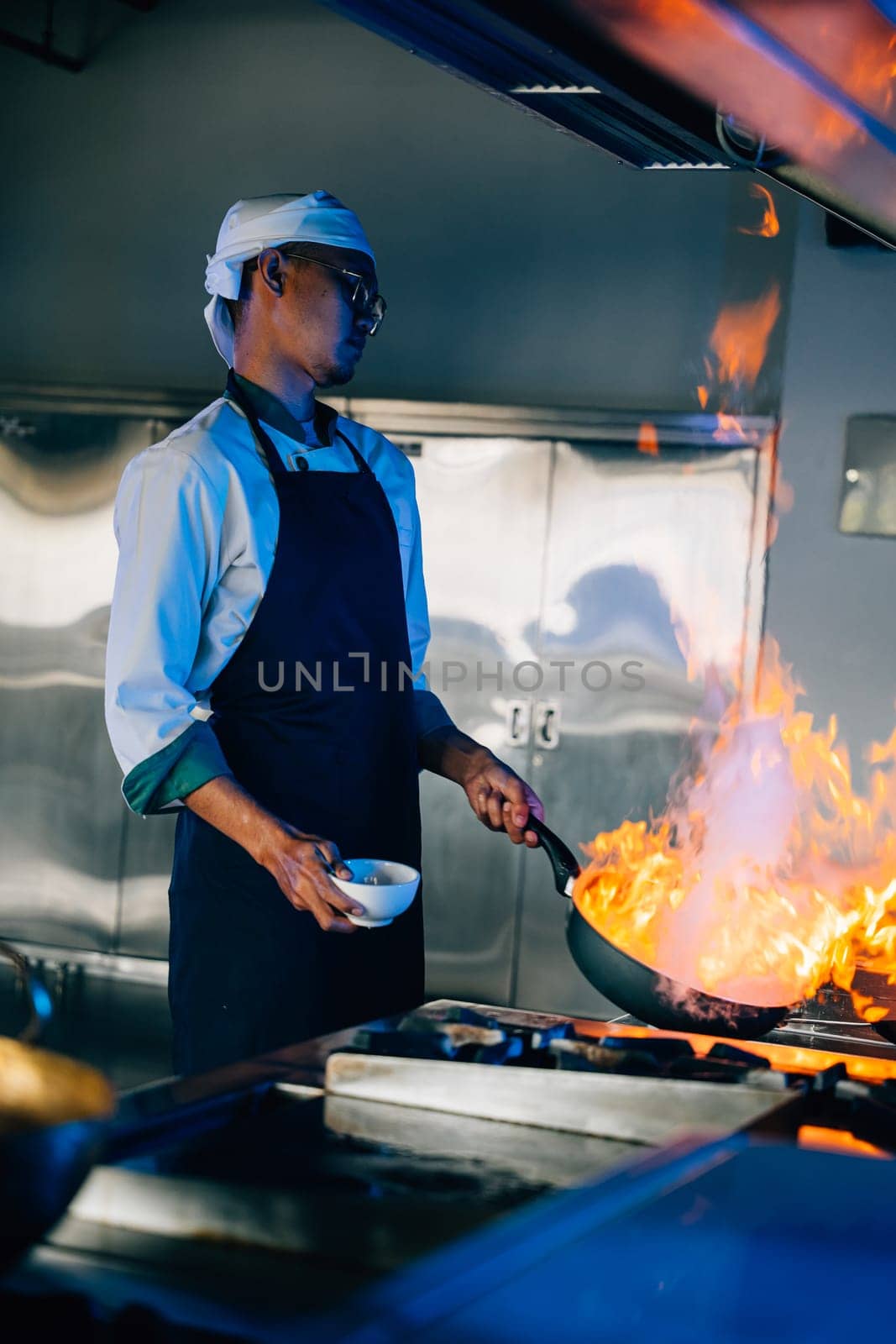 Chef hands expertly manage flaming wok in professional kitchen. Closeup of culinary skill flames cooking food. Busy chef handles flames in modern kitchen setting. cook food with fire by Sorapop