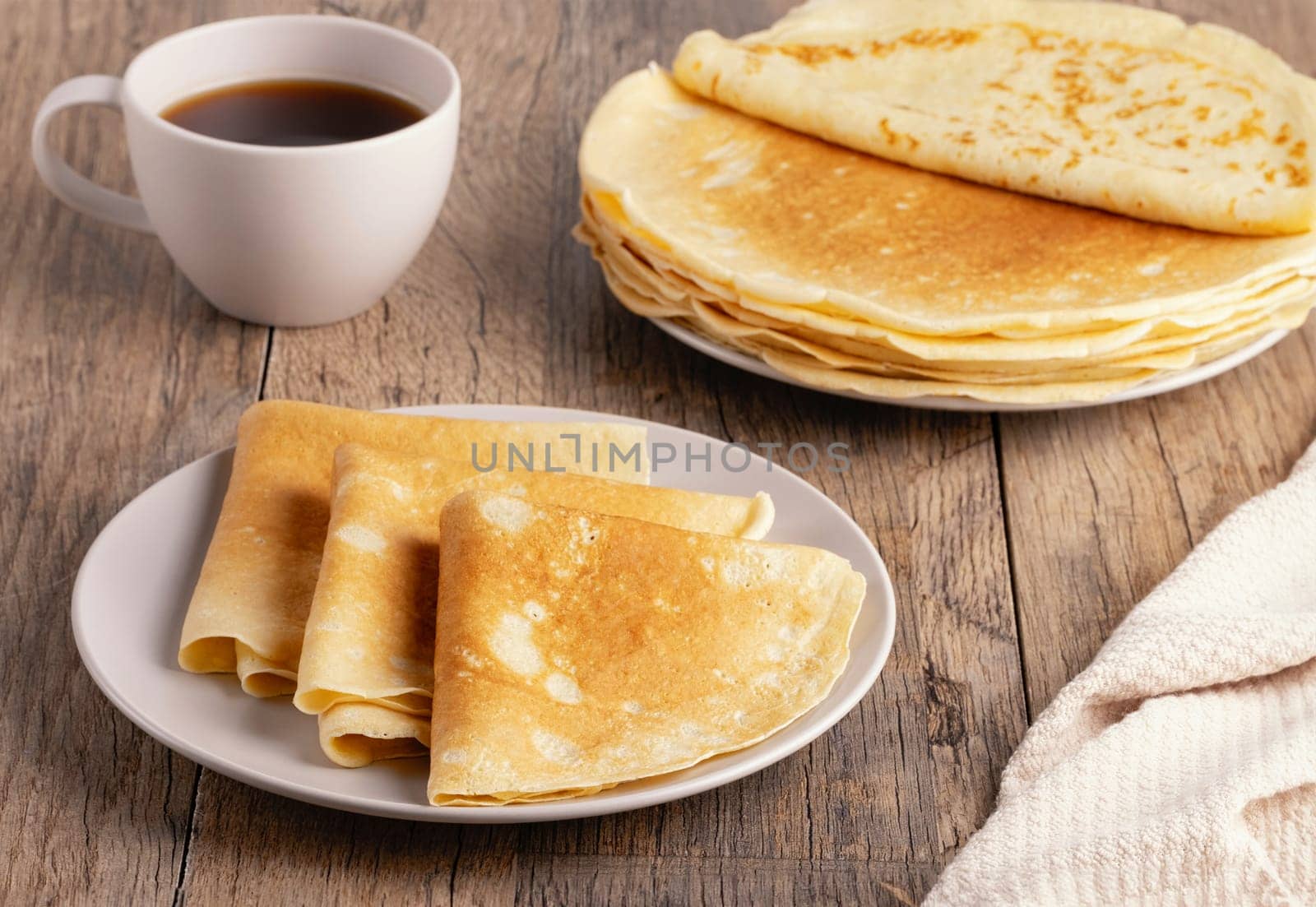 Stack of Russian thin pancakes and coffee on a wooden table.