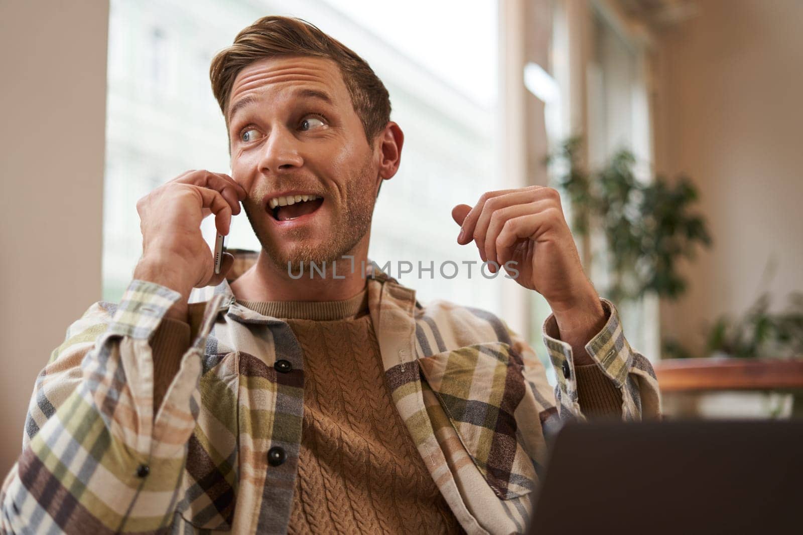 Freelance, digital nomad and workspace concept. Portrait of handsome young man with mobile phone, sitting in cafe with laptop, working on project, studying remotely, looking back outside window by Benzoix