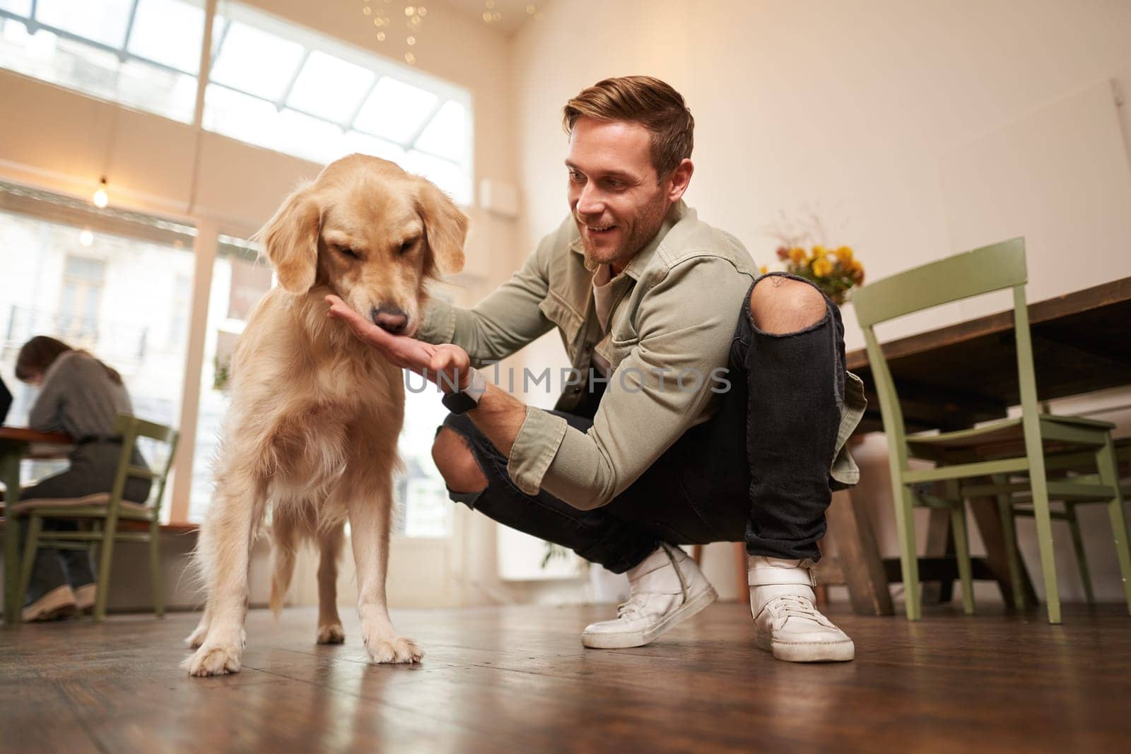 Close up portrait of happy dog owner, man with his pet giving a treat, spending time in animal-friendly cafe or co-working space by Benzoix