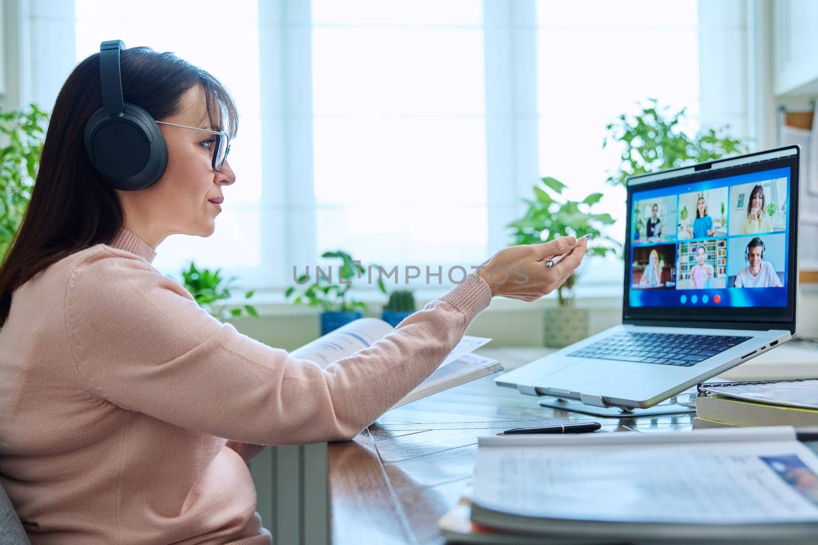 Woman teacher in headphones teaching online, high school students on computer screen by VH-studio