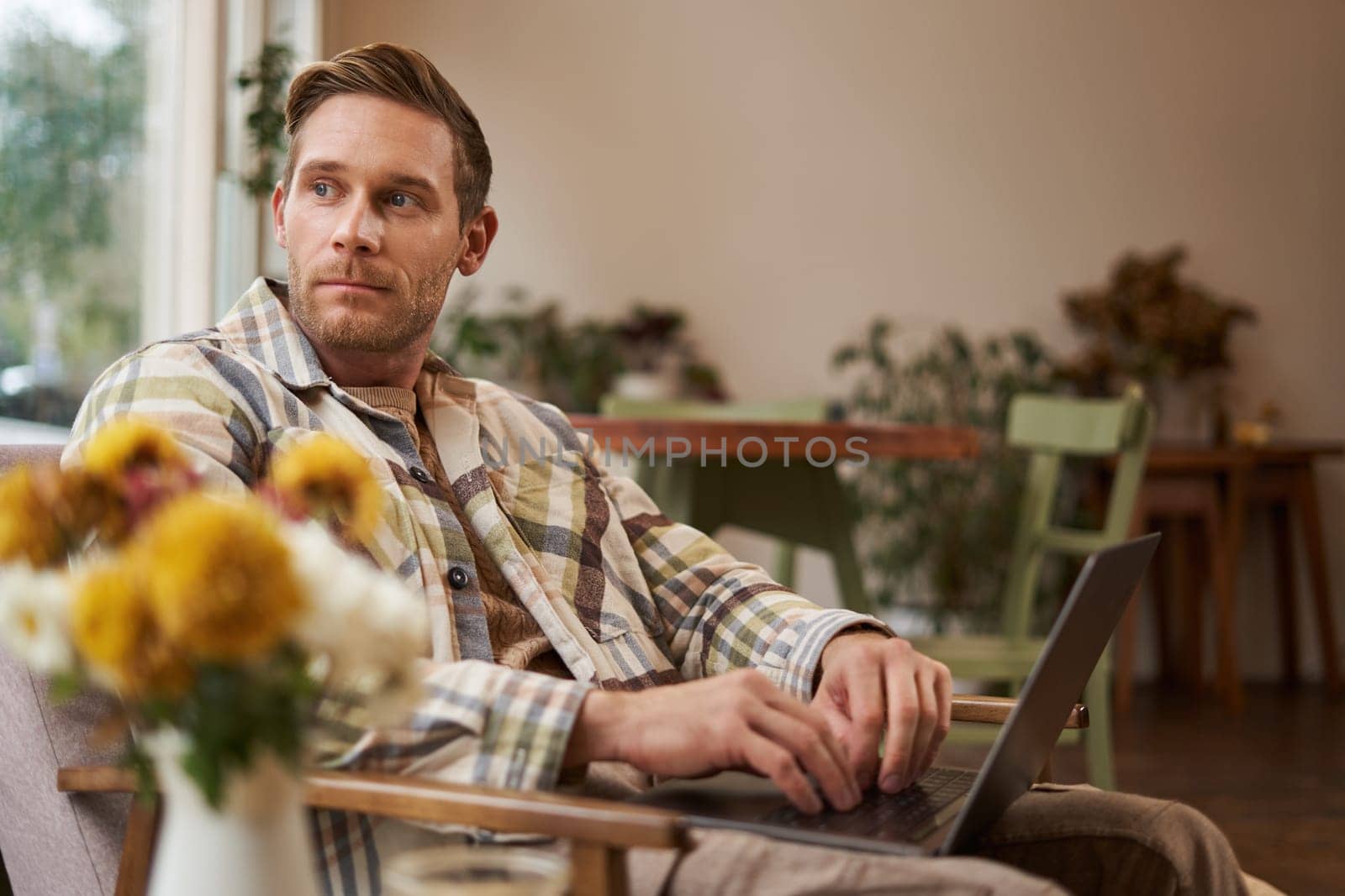 Portrait of handsome young man, working in cafe, sitting with laptop and coffee in hand, has remote job and using local co-working space instead of going to the office.