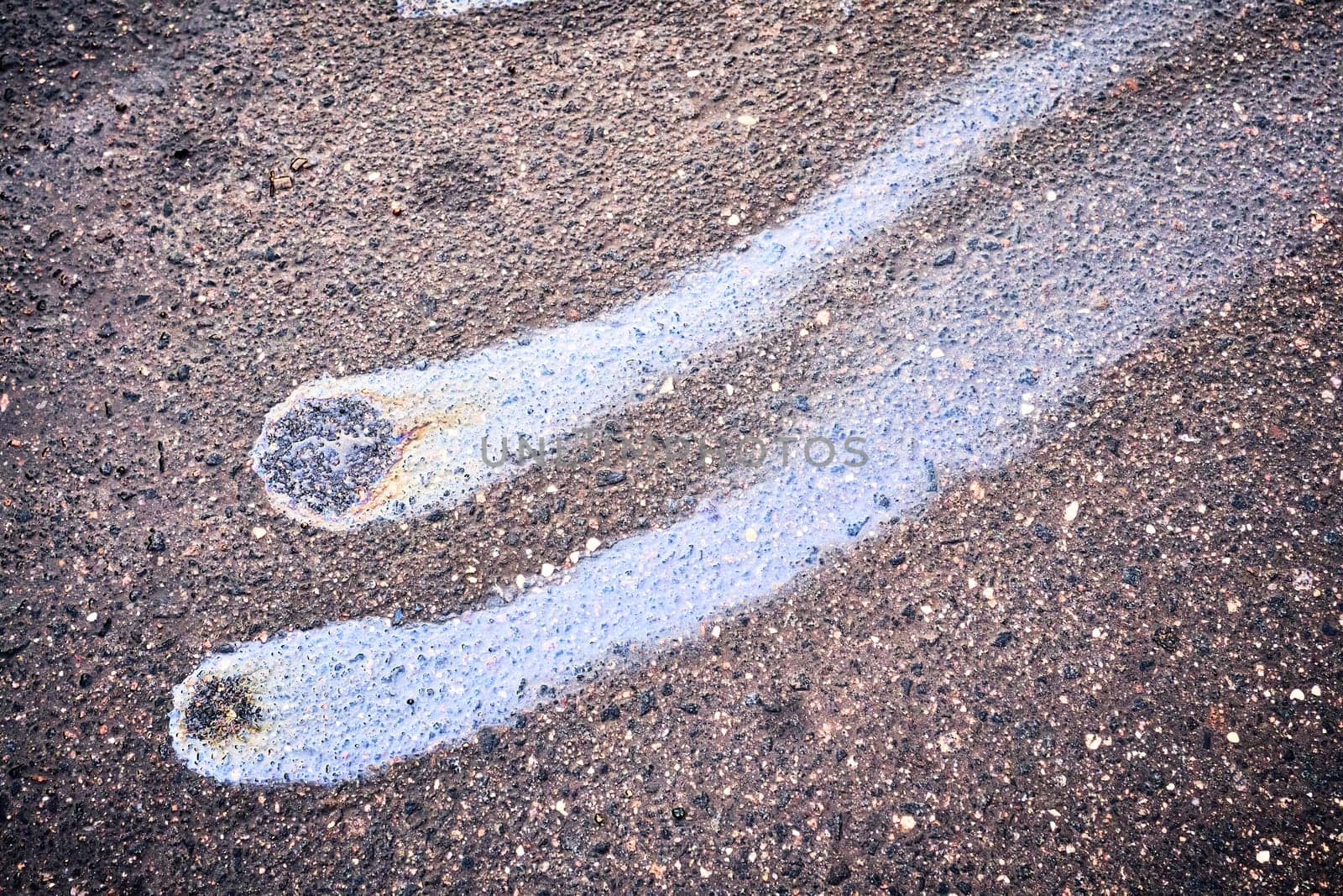 Rain blurred car oil from a malfunctioning car in a parking lot. Texture of asphalt and rainbow stains. Environmental pollution concept.