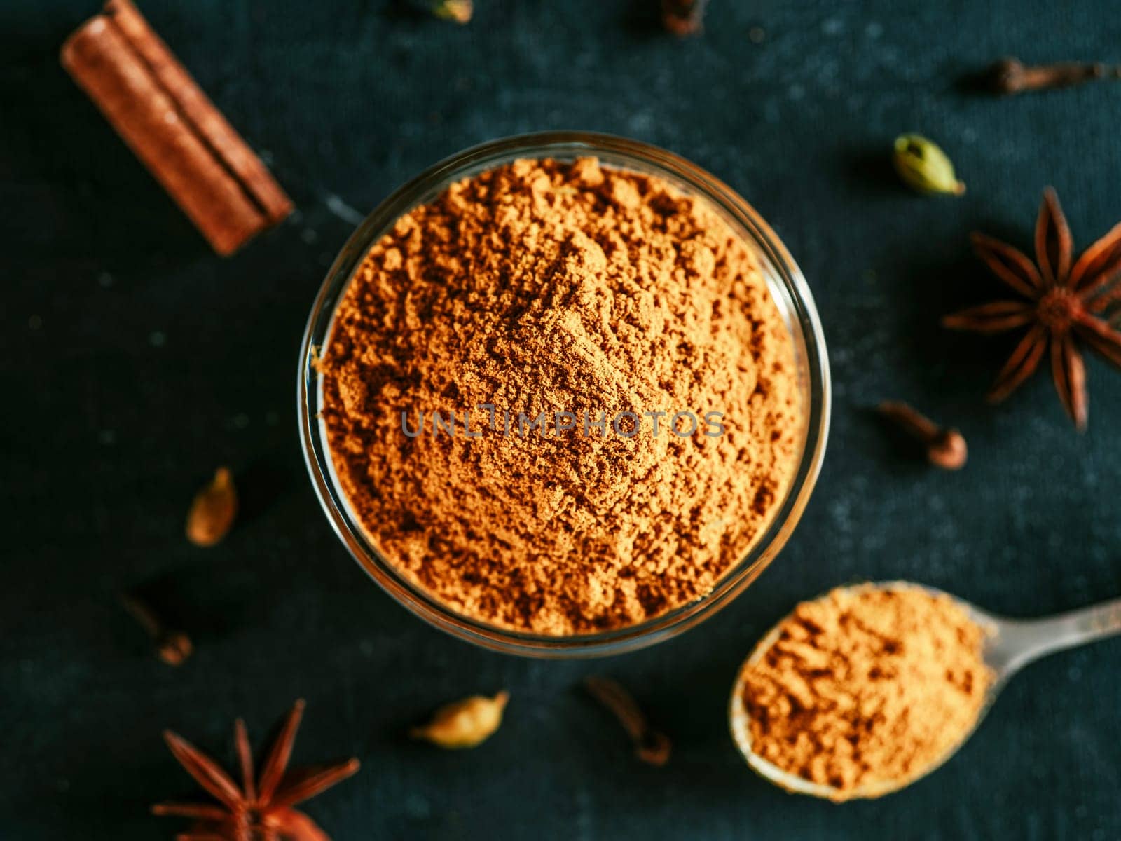 Indian or pakistani masala powder in spoon and small glass bowl. Close up view of homemade dry curry garam masala mix spices blend on dark background.