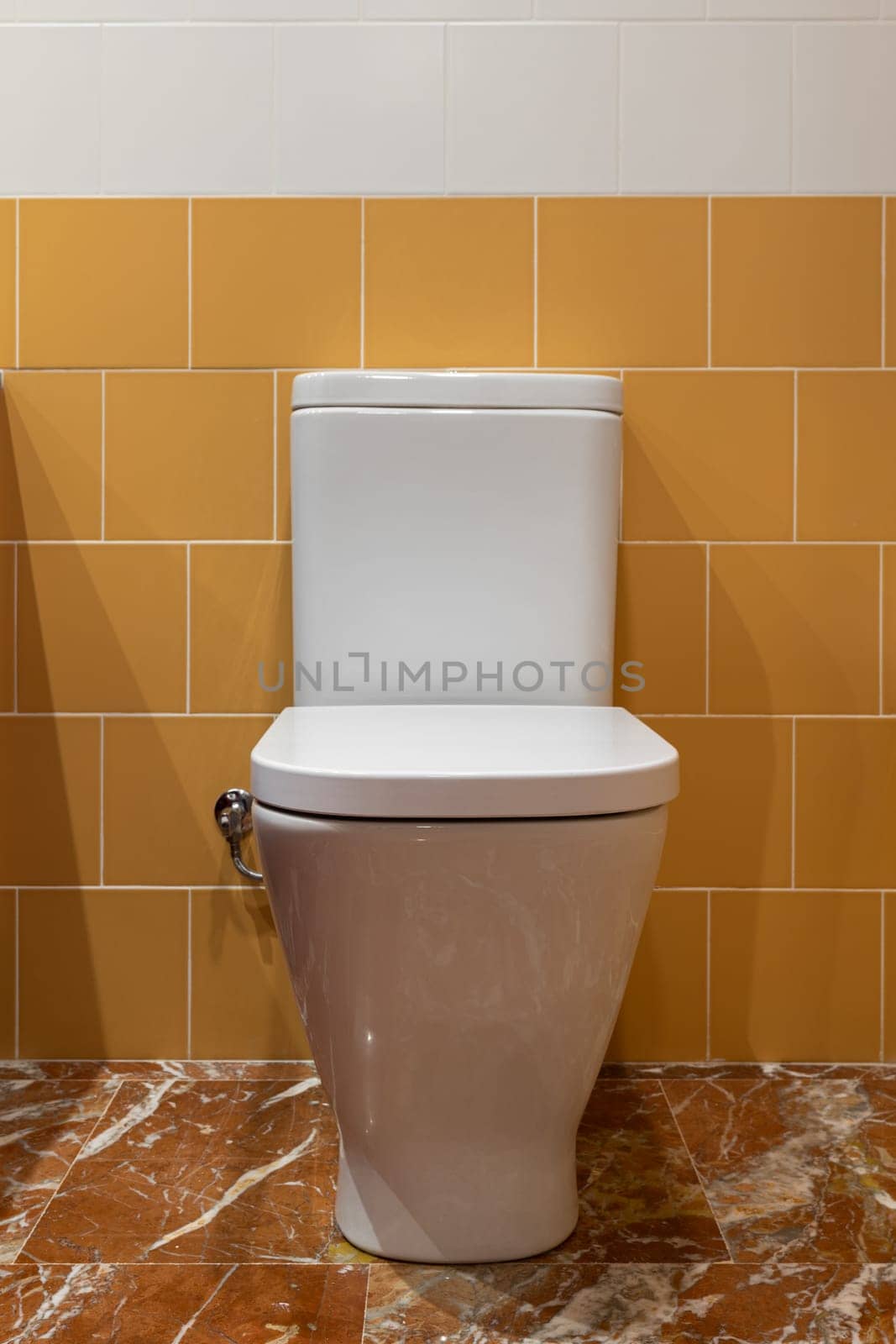 A pristine white toilet against a backdrop of orange and white tiles and marble floor by apavlin