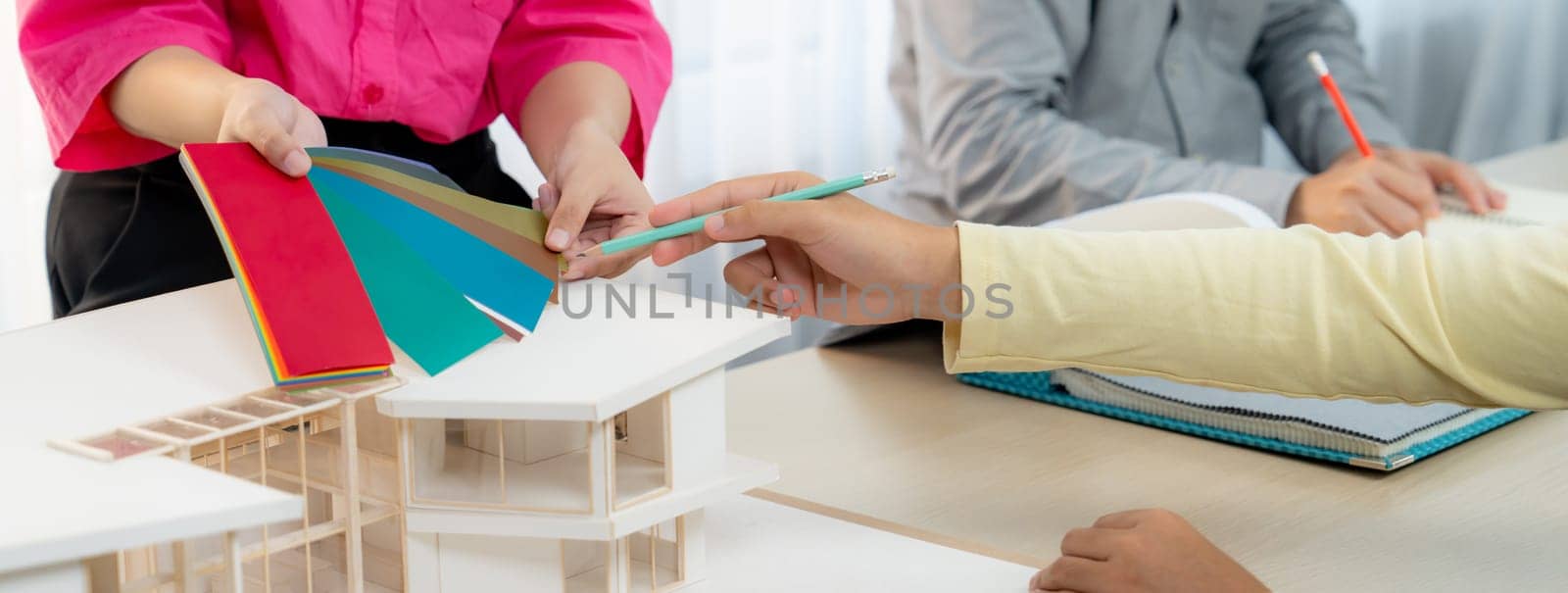 Cropped image of skilled architect and interior designer team collaborate to select house color theme at meeting room with house model placed on table. Creative working and design concept. Variegated.