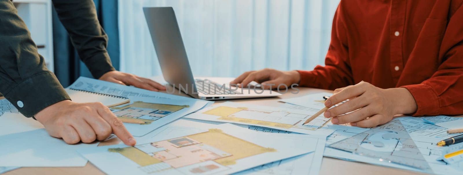 Professional architect design a blueprint by using laptop during project manager shows mistake point on table with architectural document and wooden block scatter around.. Closeup. Delineation.