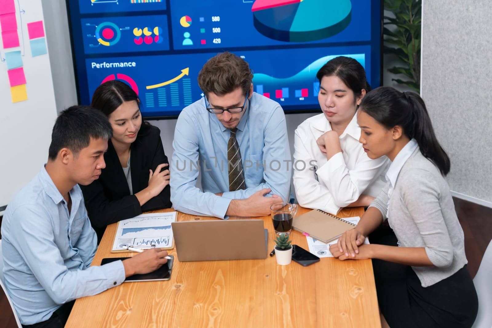 Diverse group of business analyst team analyzing financial data report. Finance data analysis chart and graph dashboard show on TV screen in meeting room for strategic marketing planning. Meticulous
