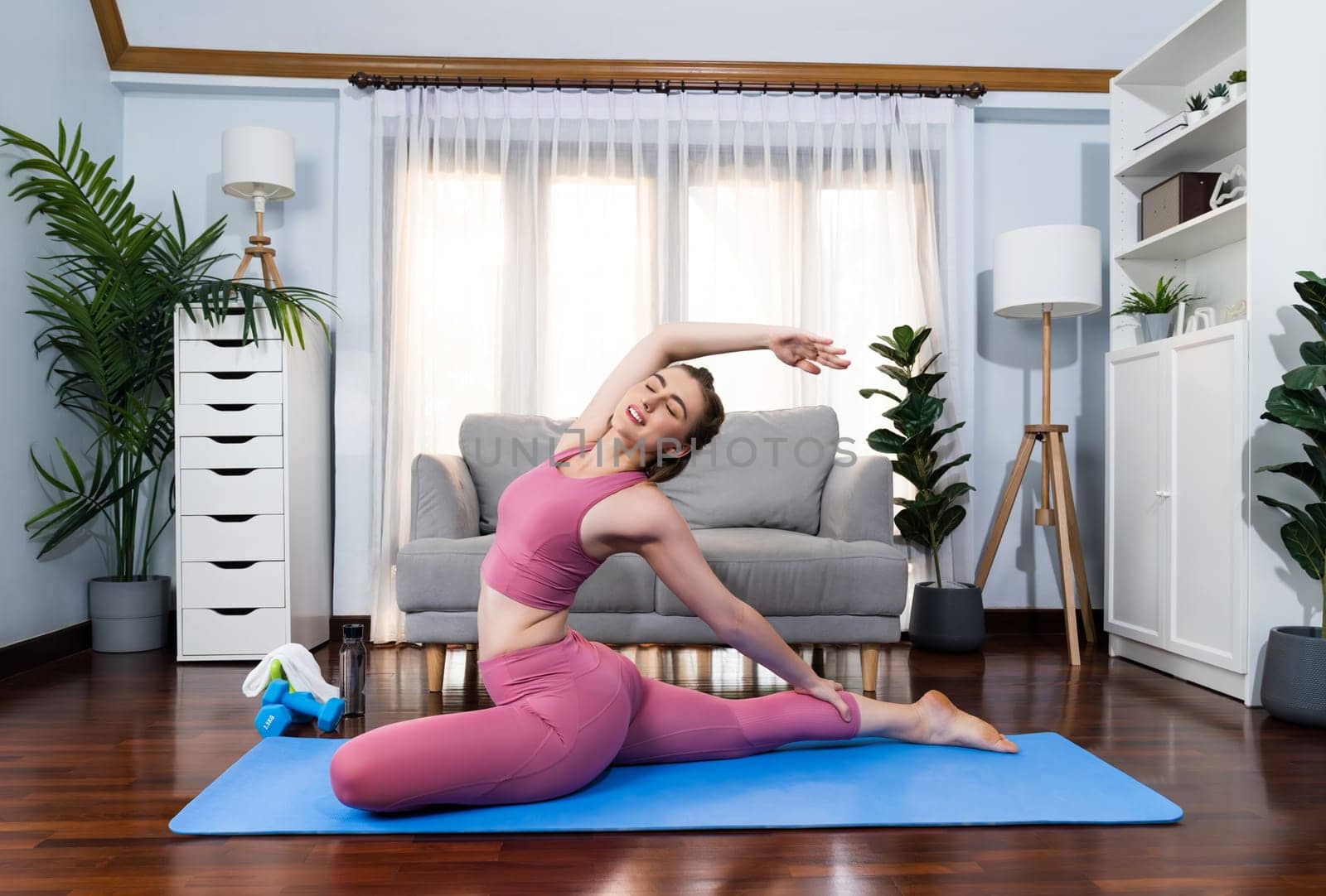 Flexible and dexterity woman in sportswear doing yoga position in meditation posture on exercising mat at home. Healthy gaiety home yoga lifestyle with peaceful mind and serenity.