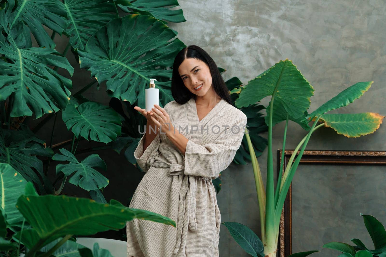 Tropical and exotic spa garden with bathtub in modern hotel or resort with woman in bathrobe holding beauty skincare product while enjoying leisure lush with greenery foliage background. Blithe