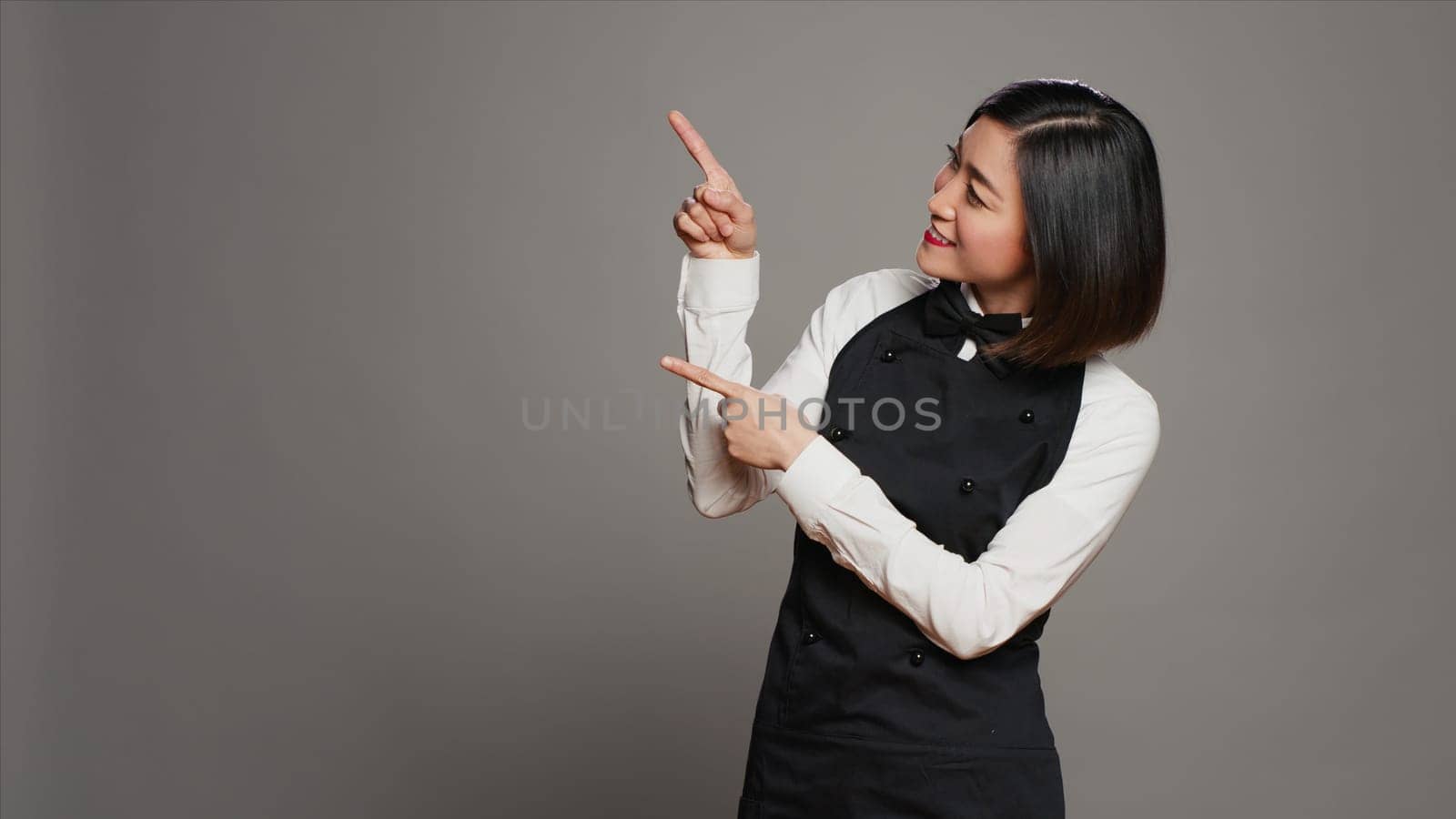 Asian waitress pointing up for an advertisement in studio by DCStudio