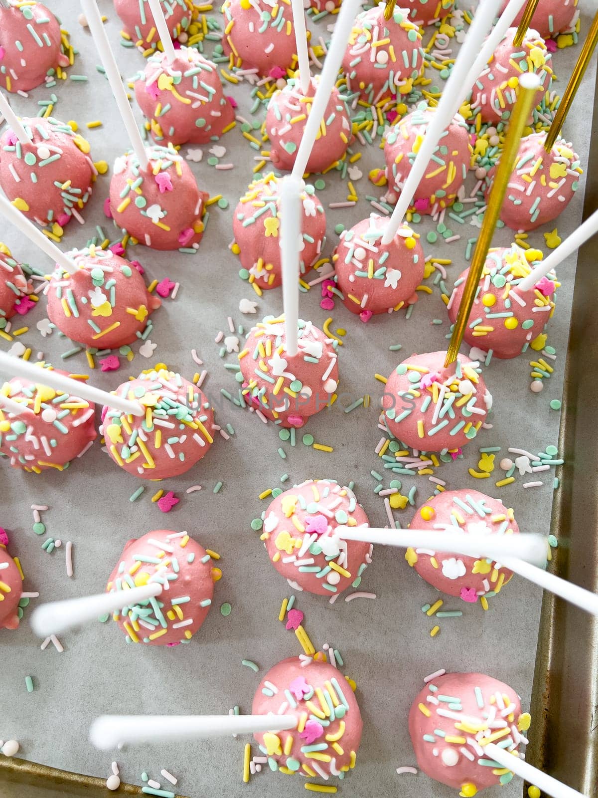 Arrayed neatly on parchment, these hand-dipped pink cake pops are a playful treat, adorned with a rainbow of sprinkles that add a festive touch to the sweet delights.