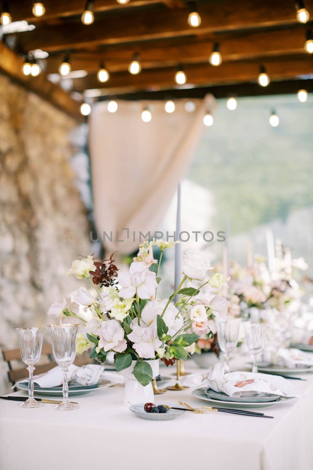 Bouquet of flowers stands on a festive table on a terrace with glowing garlands. High quality photo