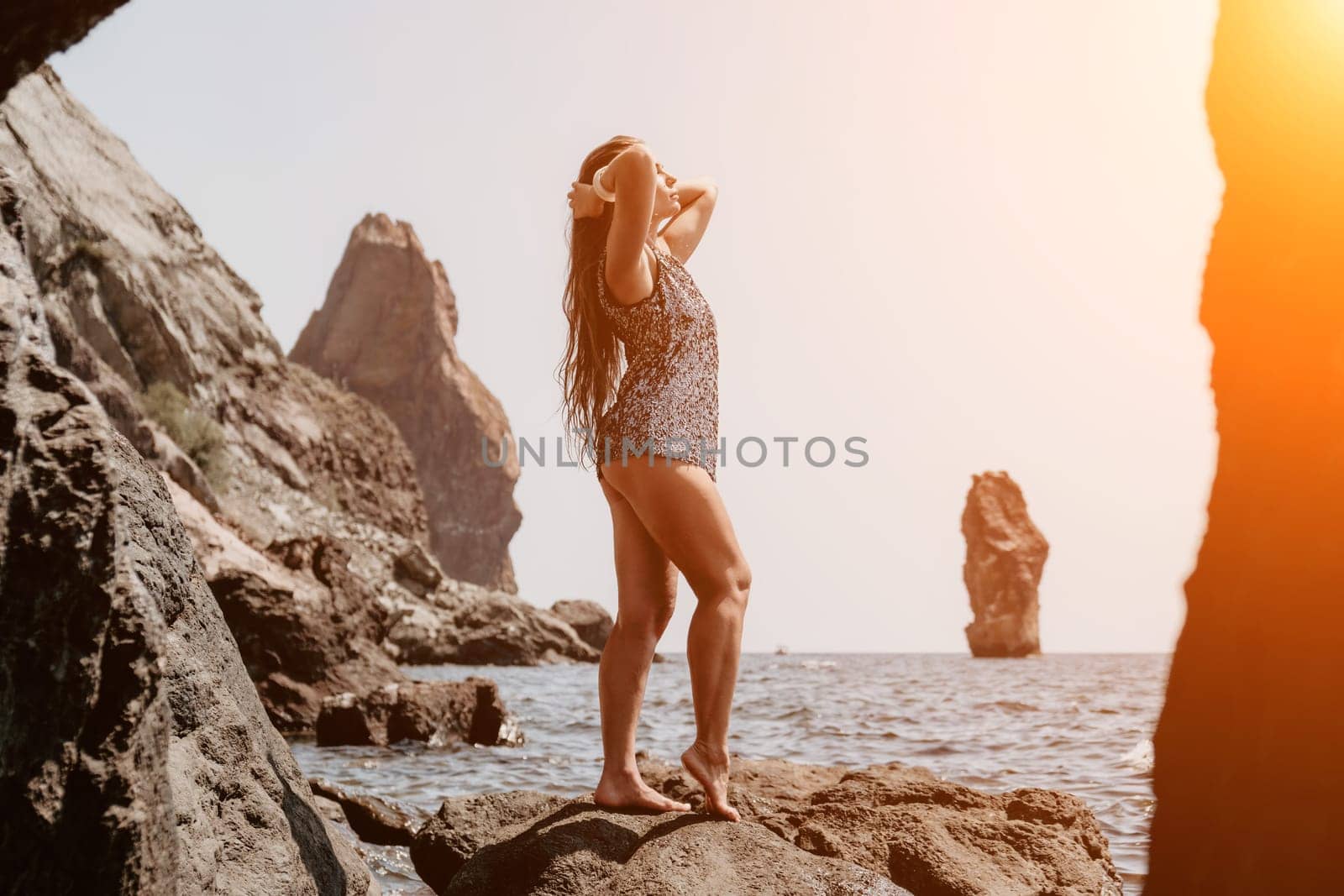 Woman travel sea. Young Happy woman in a long red dress posing on a beach near the sea on background of volcanic rocks, like in Iceland, sharing travel adventure journey