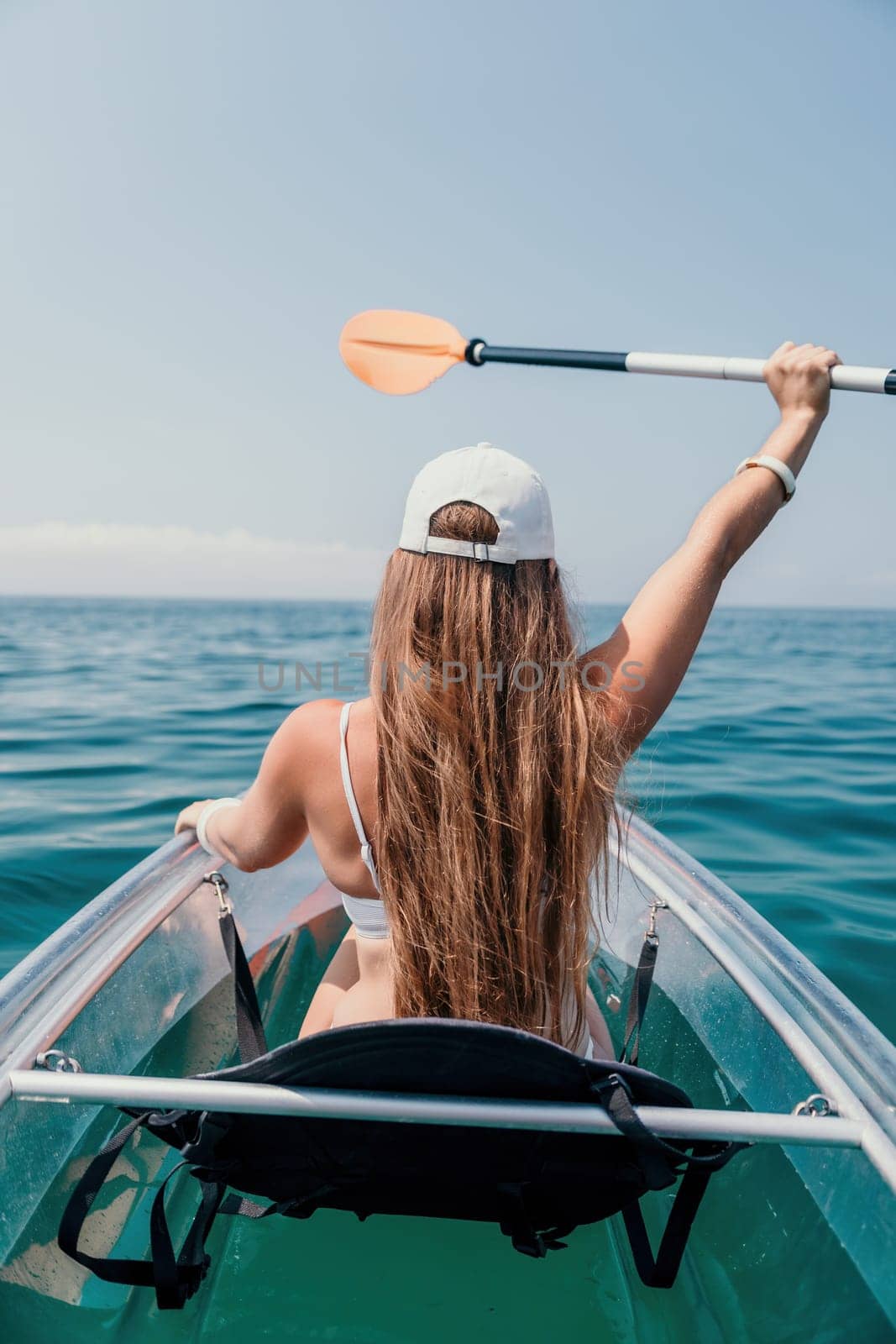 Woman in kayak back view. Happy young woman with long hair floating in transparent kayak on the crystal clear sea. Summer holiday vacation and cheerful female people relaxing having fun on the boat by panophotograph