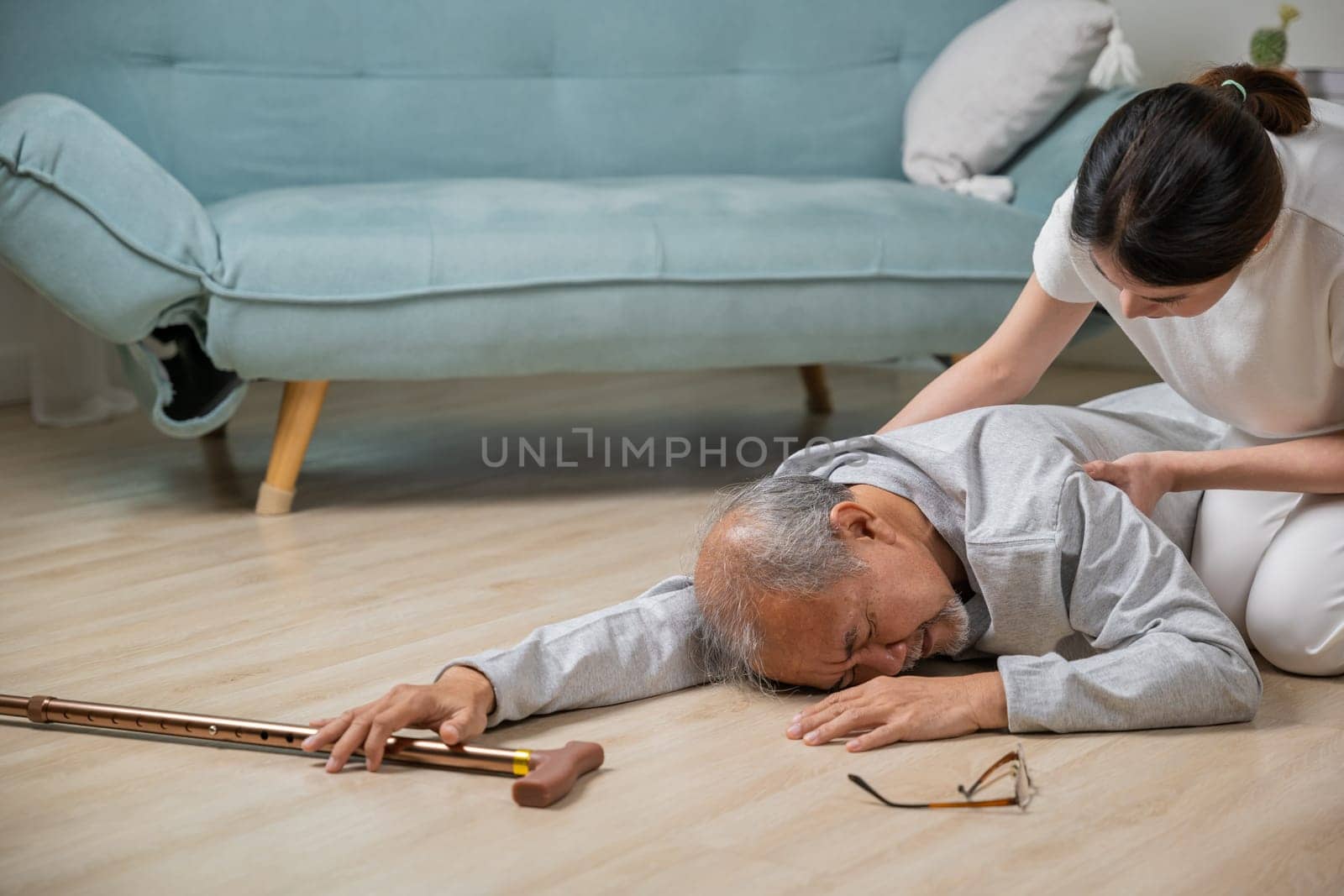 old man falling down lying on floor with walking stick and assistant nurse help to support by Sorapop