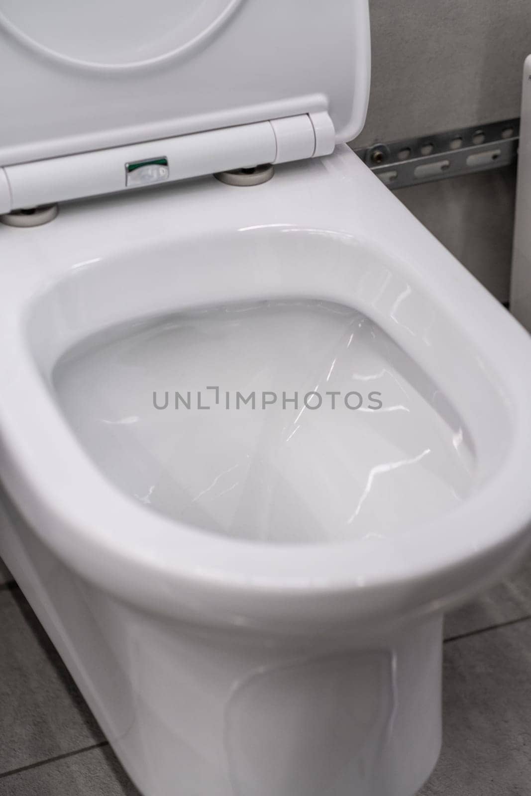 A white toilet, a bathroom fixture, sits on a tiled floor in a rectangleshaped bathroom. The toilet is made of composite material and is a necessary bathroom accessory