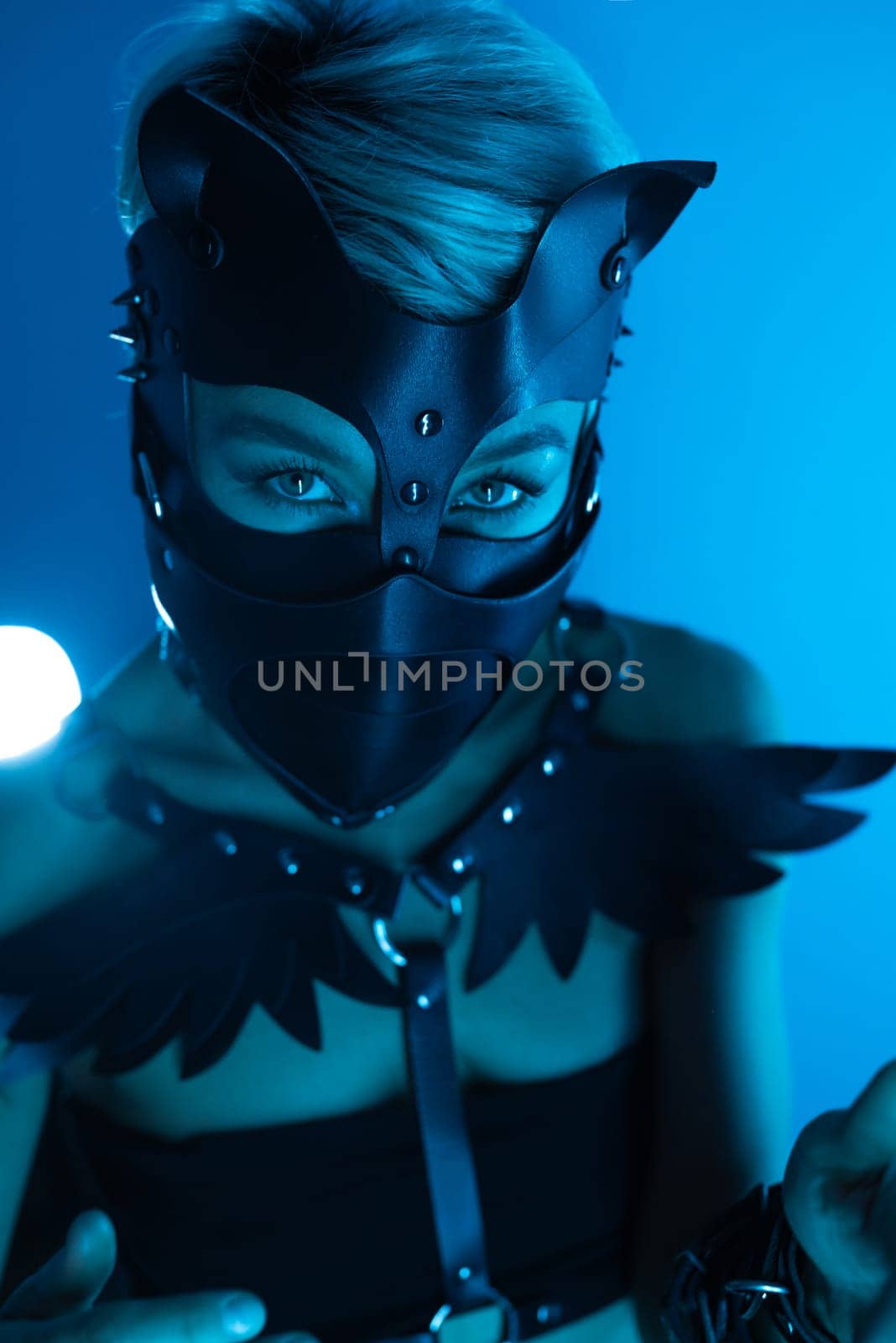 portrait of a hot sexy girl in a leather cat mask and muzzled in bdsm handcuffs on neon blue light background