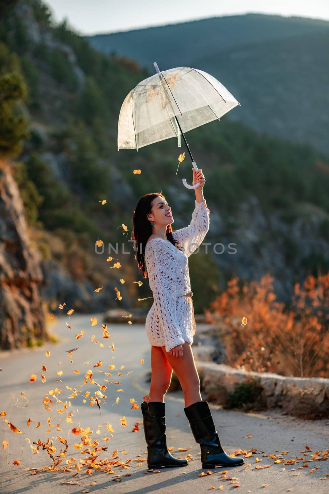 woman umbrella leaves , She holds him over her head, autumn leaves are falling out of him. Beautiful woman in a dress with an umbrella in the autumn park on the road in the mountains