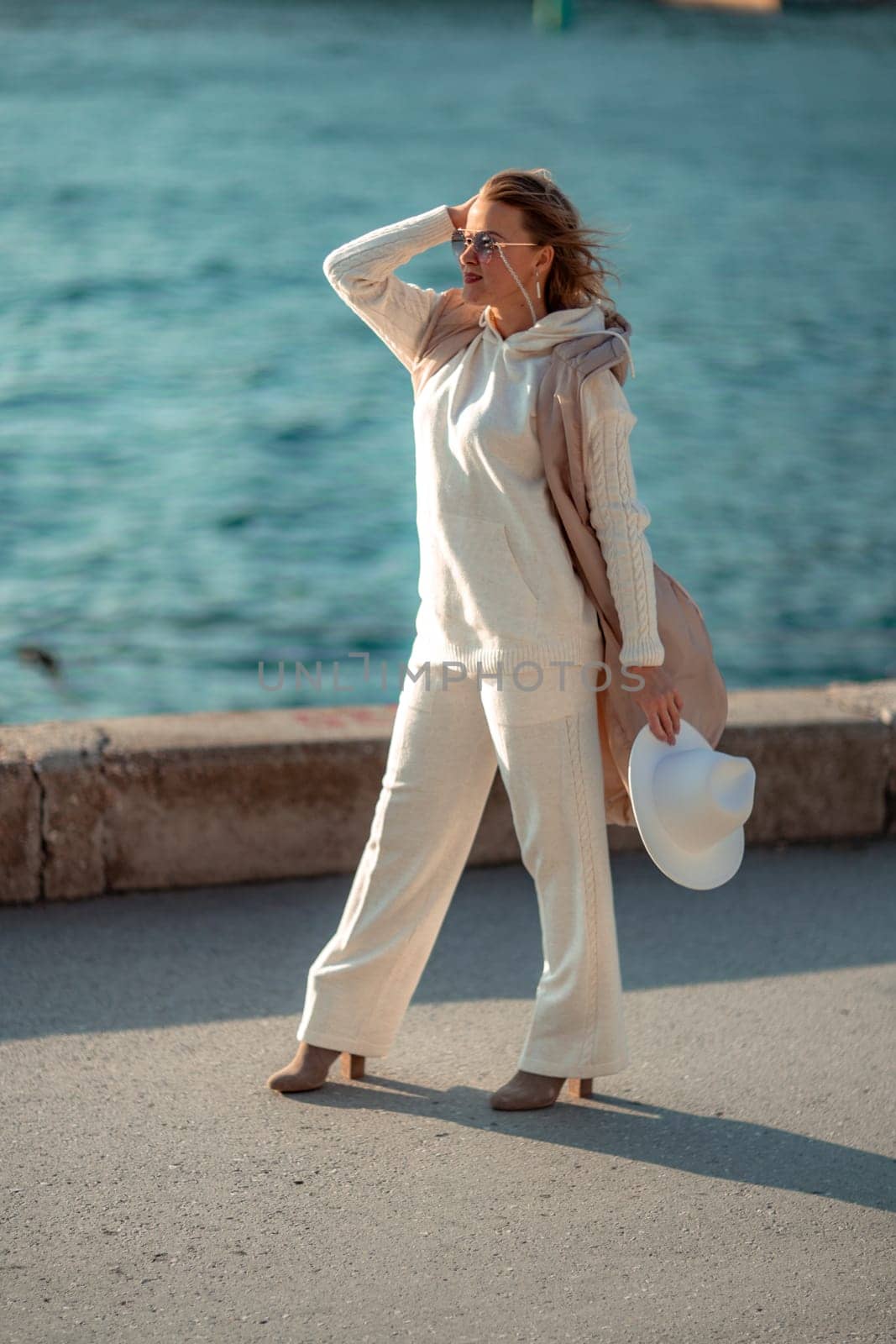 Happy blonde woman in a white suit and hat posing at the camera against the backdrop of the sea by Matiunina