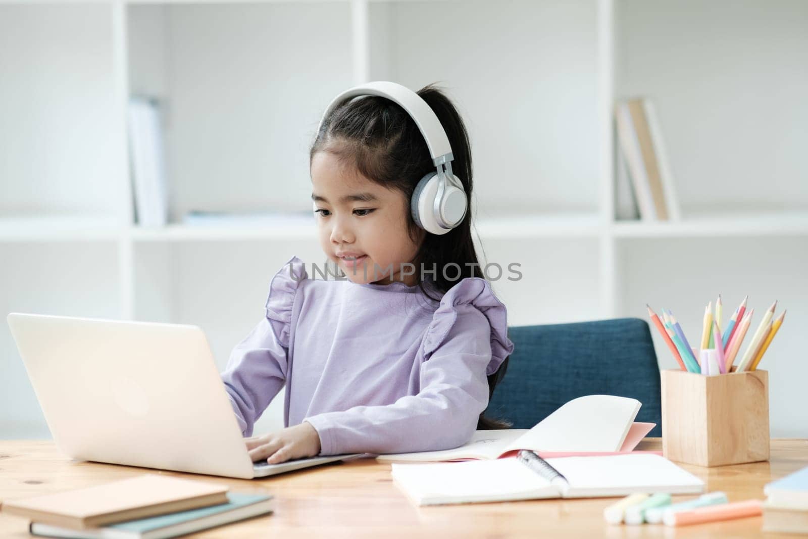 A young girl is sitting at a desk with a laptop and headphones on. She is focused on her work and she is enjoying herself