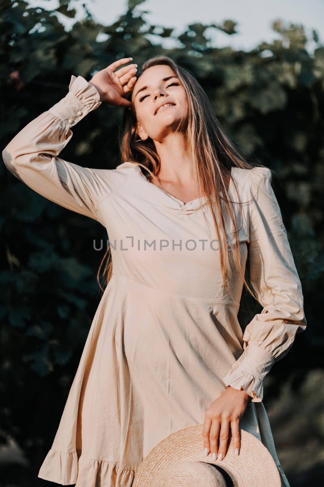 Woman stands in front of vineyard. She is wearing a light dress and posing for a photo. Travel concept to different countries.