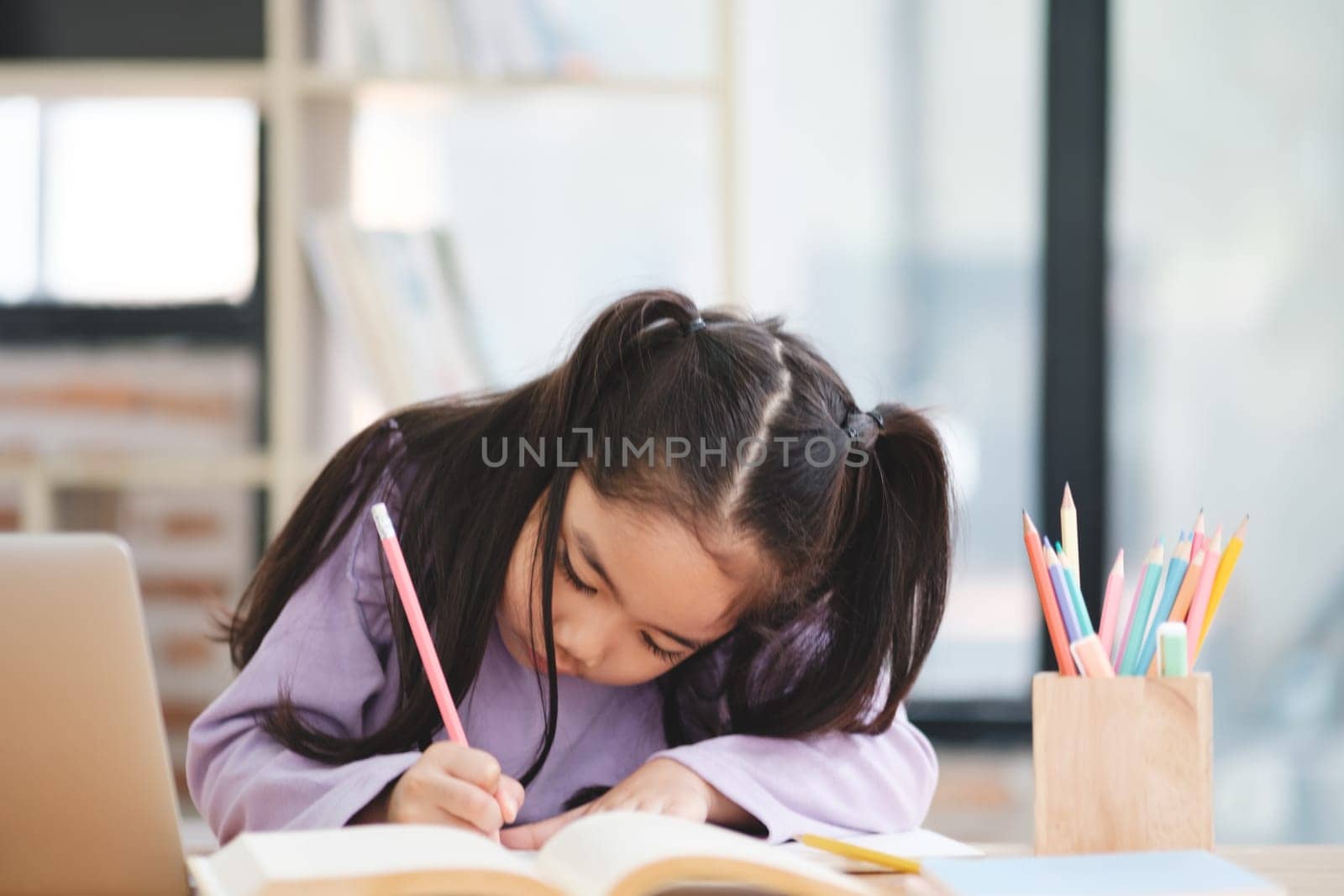 A young girl is sitting at a desk with a pencil and a book by ijeab