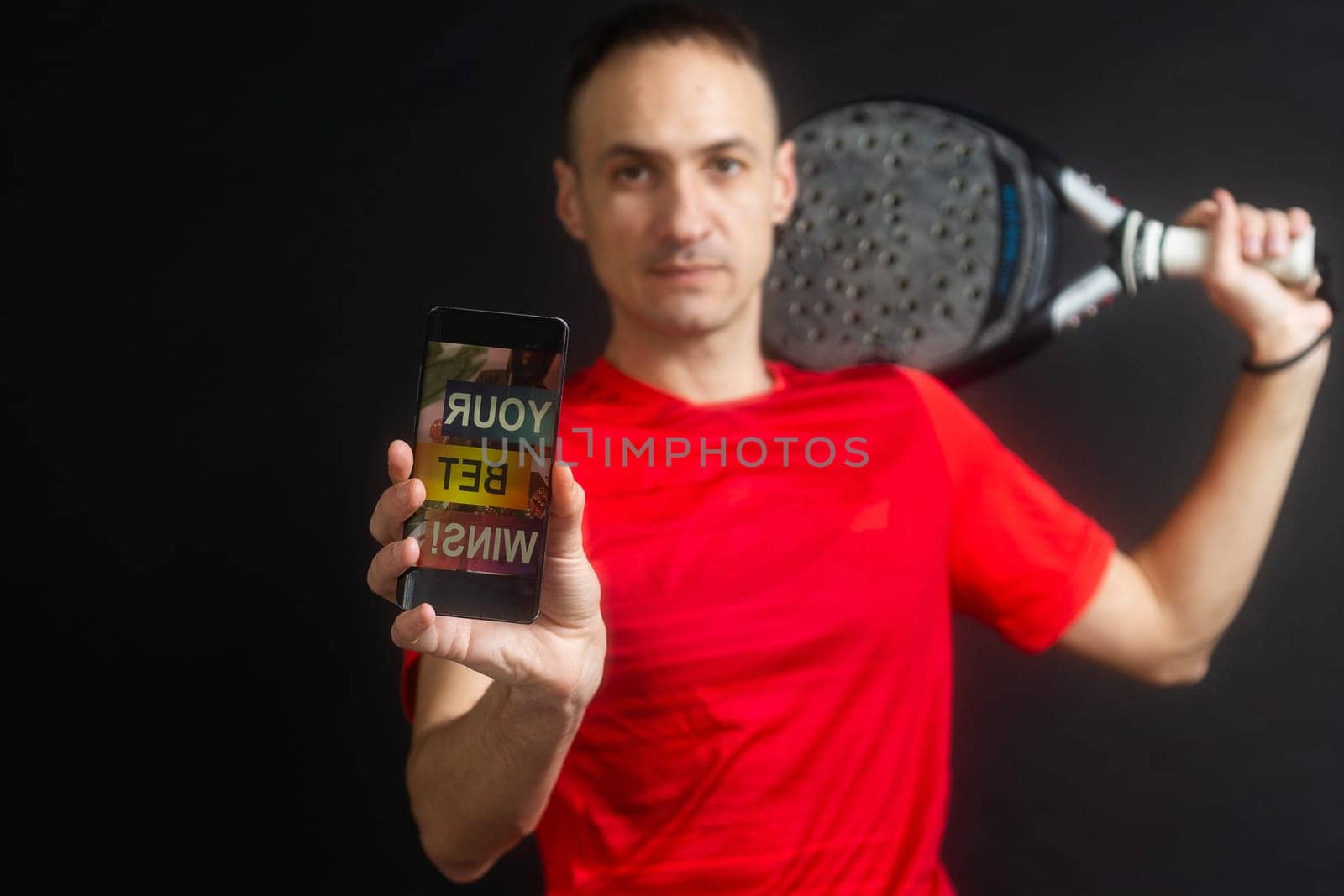 man holding paddel racket and smartphone with sports betting on black background. High quality photo