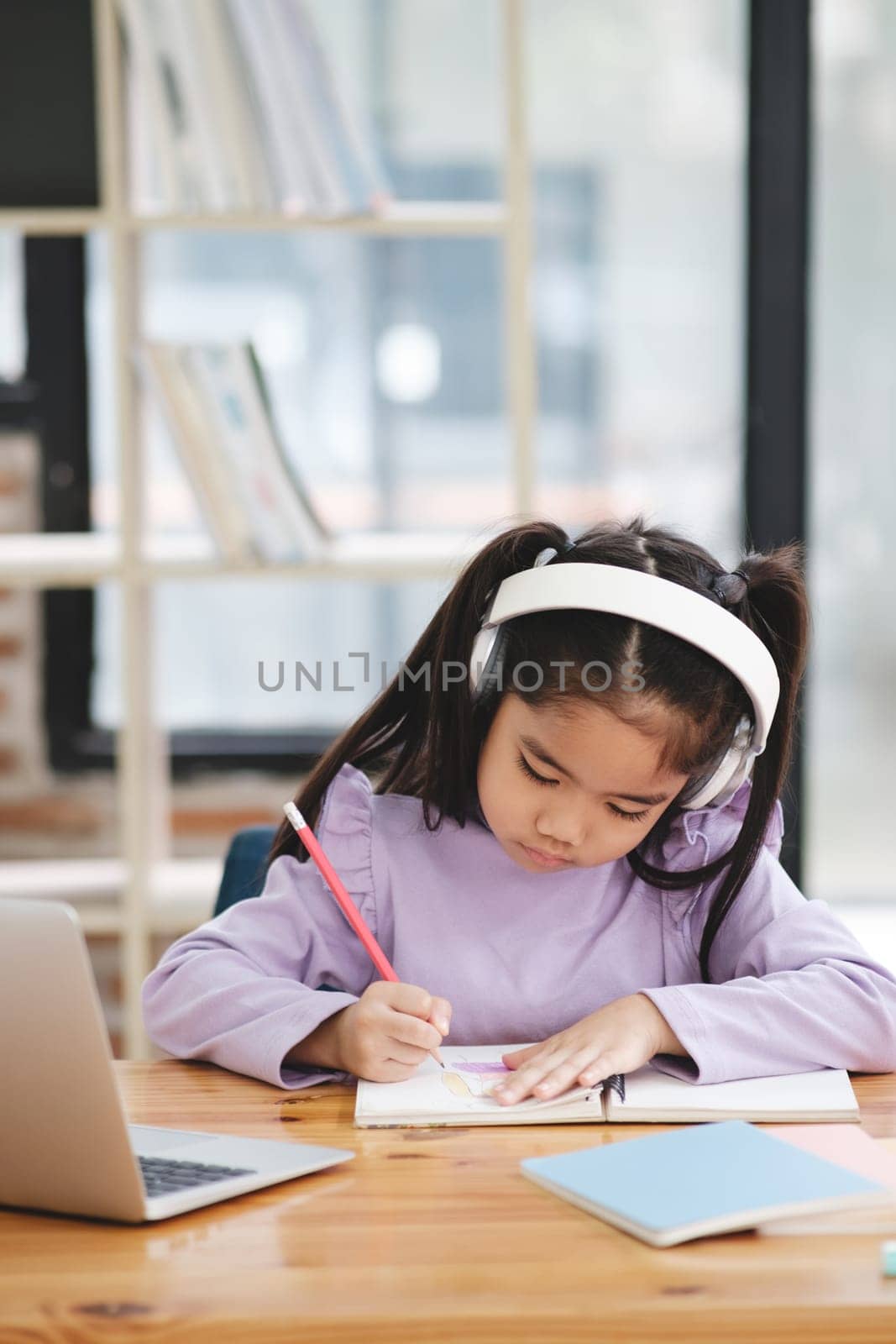 A young girl is sitting at a desk with a laptop and a notebook by ijeab