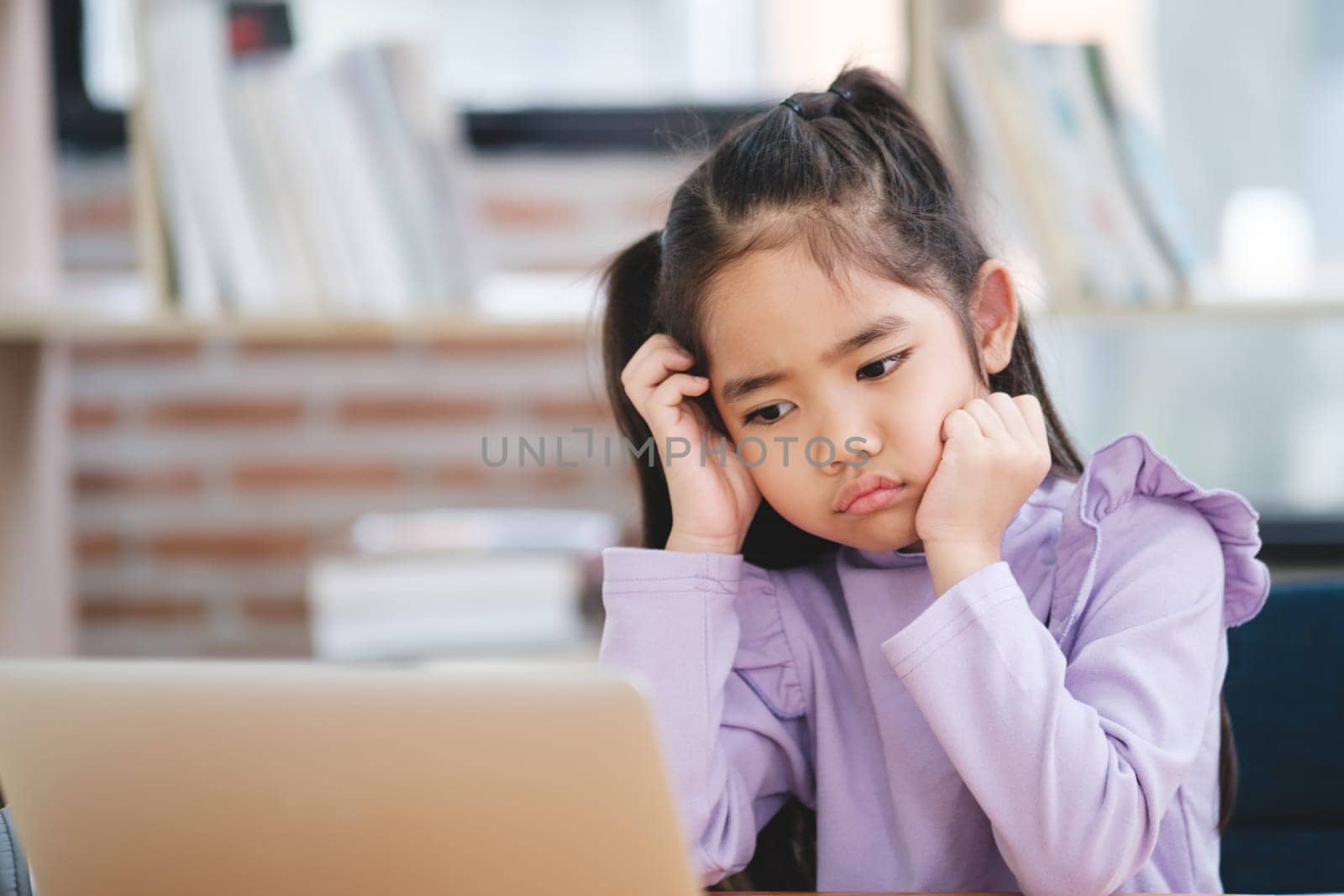 A young student appears disinterested and bored while engaging with an online class on her laptop.