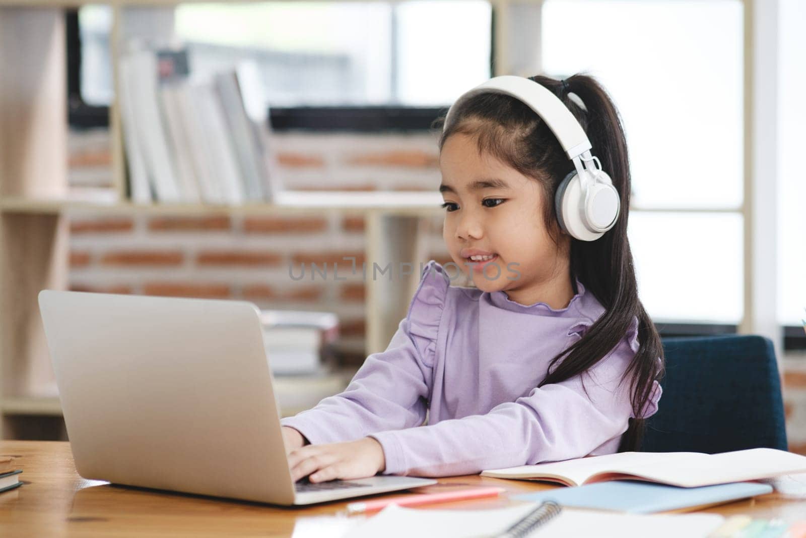 A young girl is sitting at a desk with a laptop and headphones on. She is smiling and she is enjoying her work