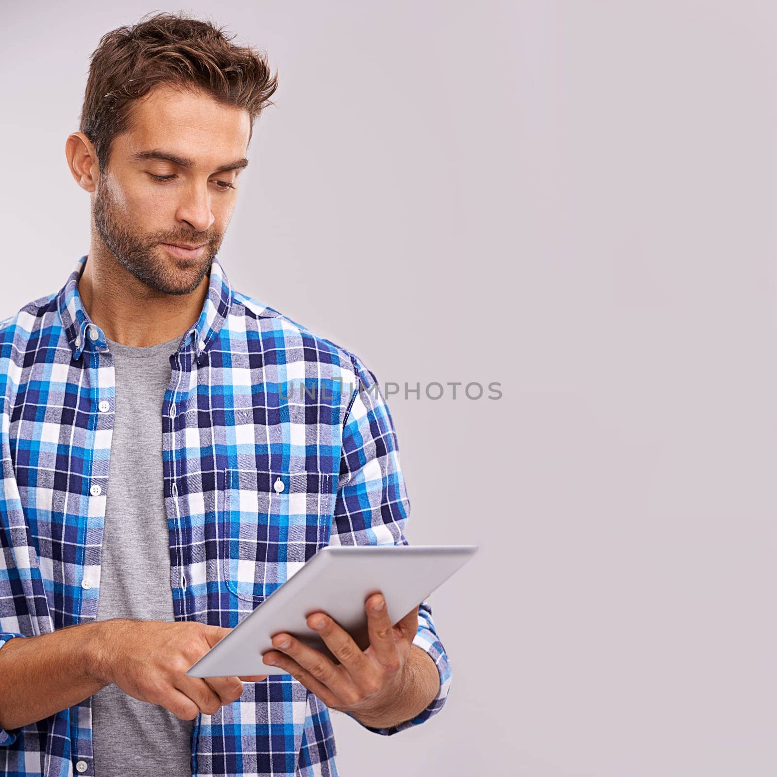 Typing, tablet and man with connection, internet and digital app on a grey studio background. Person, mockup space and model with technology or communication with social media and website information by YuriArcurs