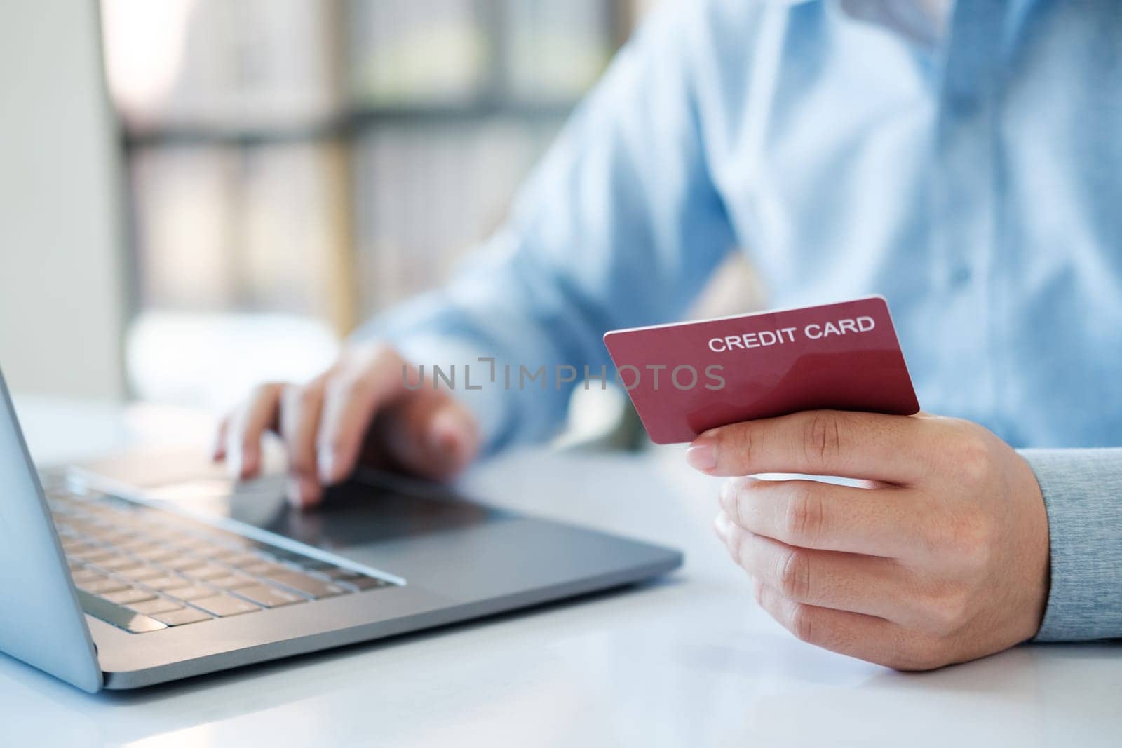 A man is using a laptop to pay for something with a red credit card. Concept of convenience and ease, as the man is able to complete his transaction quickly and easily using his laptop