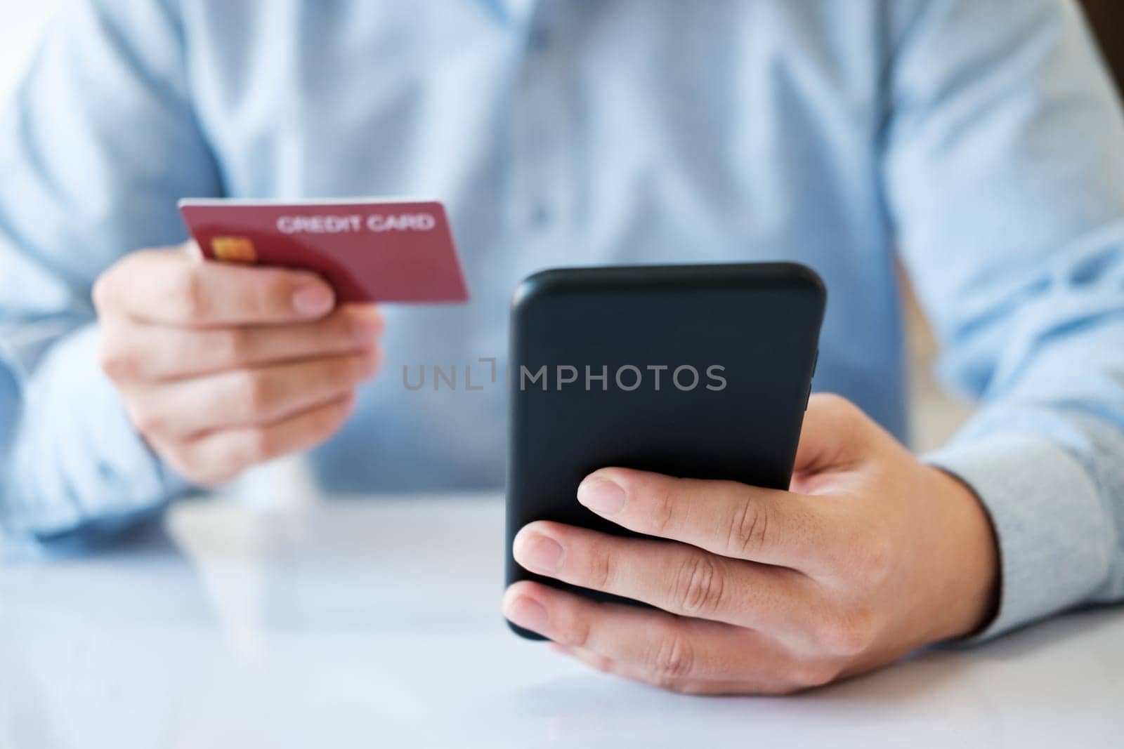 A man is using his phone to pay for a credit card. He is holding the credit card in one hand and the phone in the other