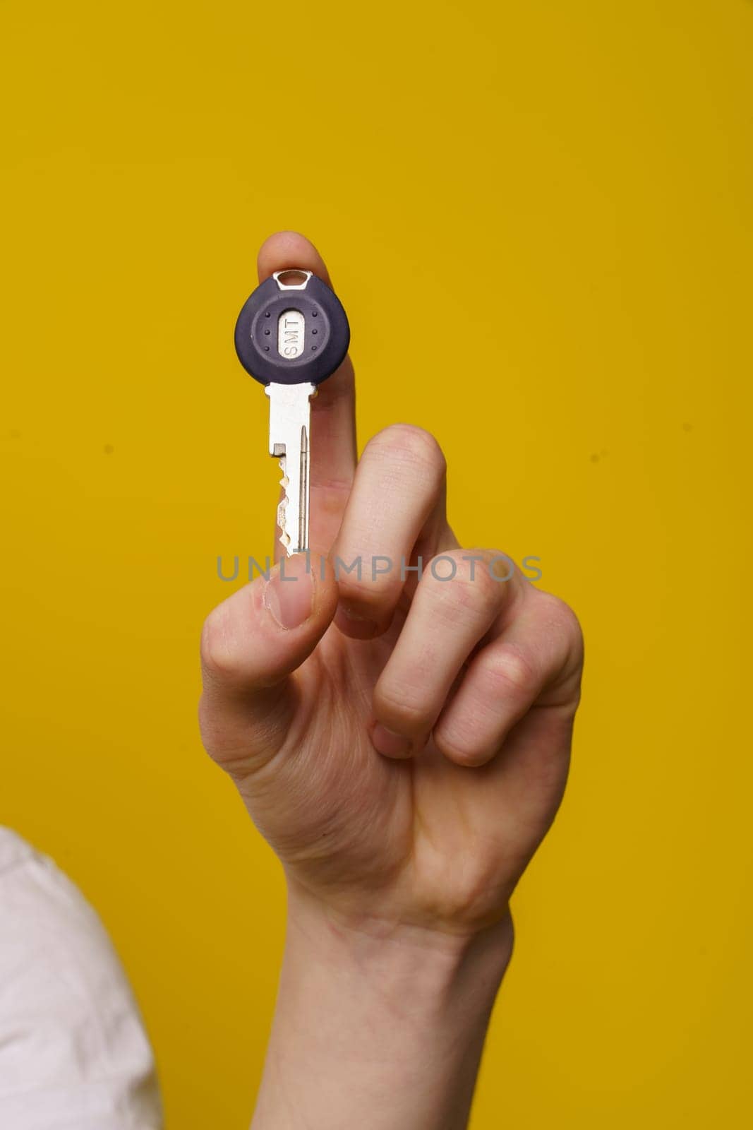 Close-up image of a man hand holding home key with isolated yellow background and copy space. Perfect for conveying concepts of homeownership, real estate, property, and security. by LipikStockMedia