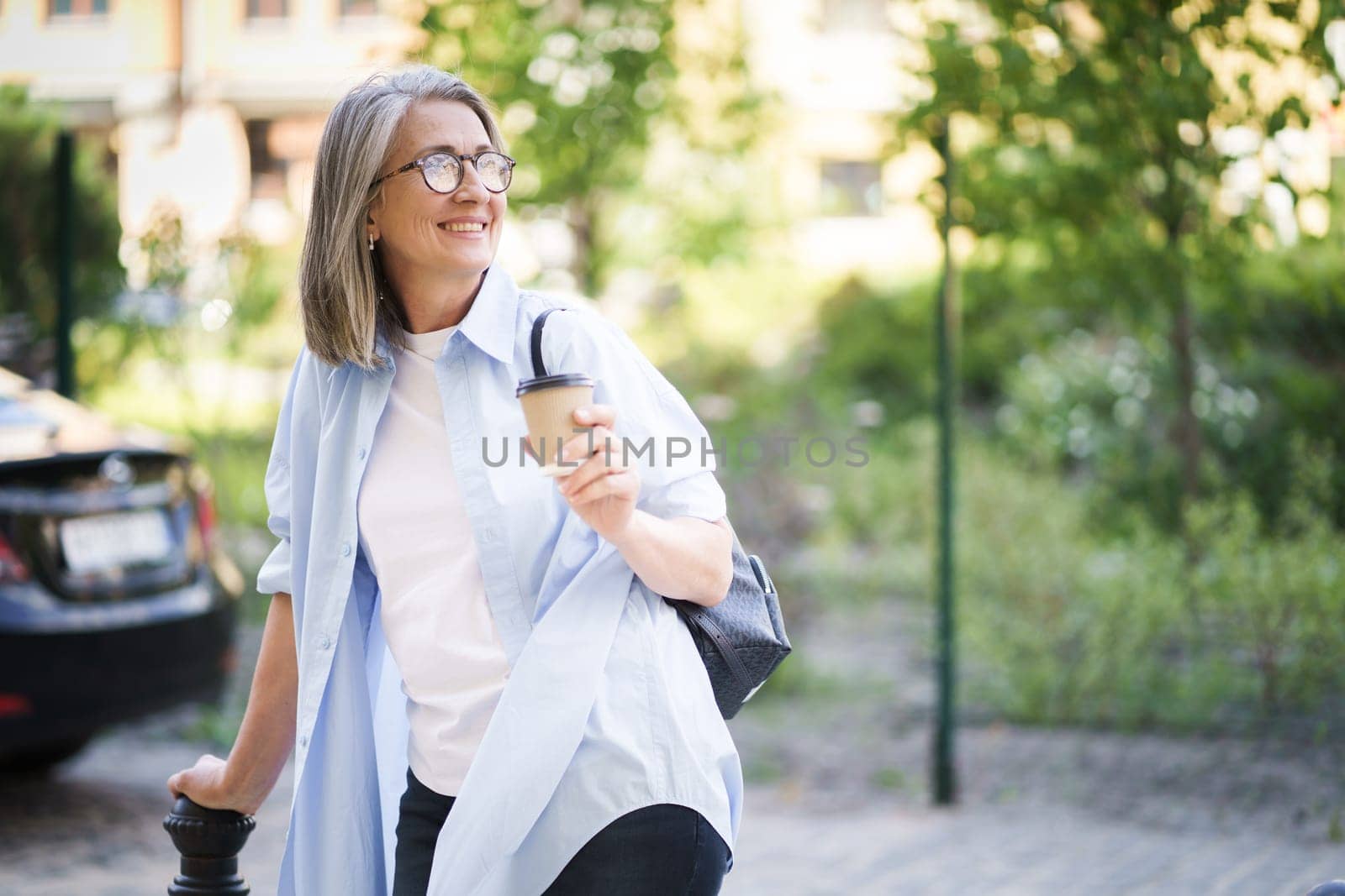 A woman is walking down a street, clutching a cup of coffee in her hand.