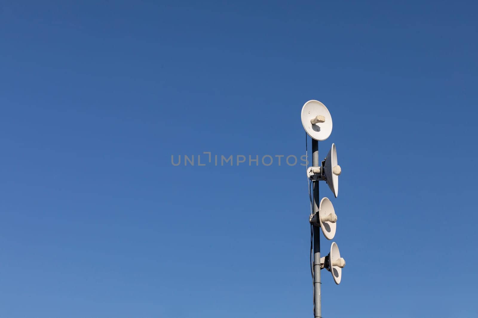 White telecommunications antennas on a single mast high above the city against the background of a blue sky. Technology of digital sending and receiving of data packets.