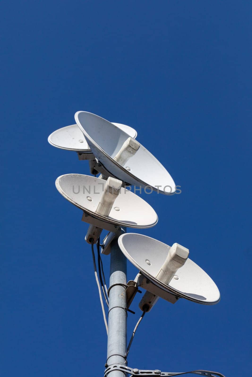White telecommunications antennas on a single mast high above the city against the background of a blue sky. Technology of digital sending and receiving of data packets.