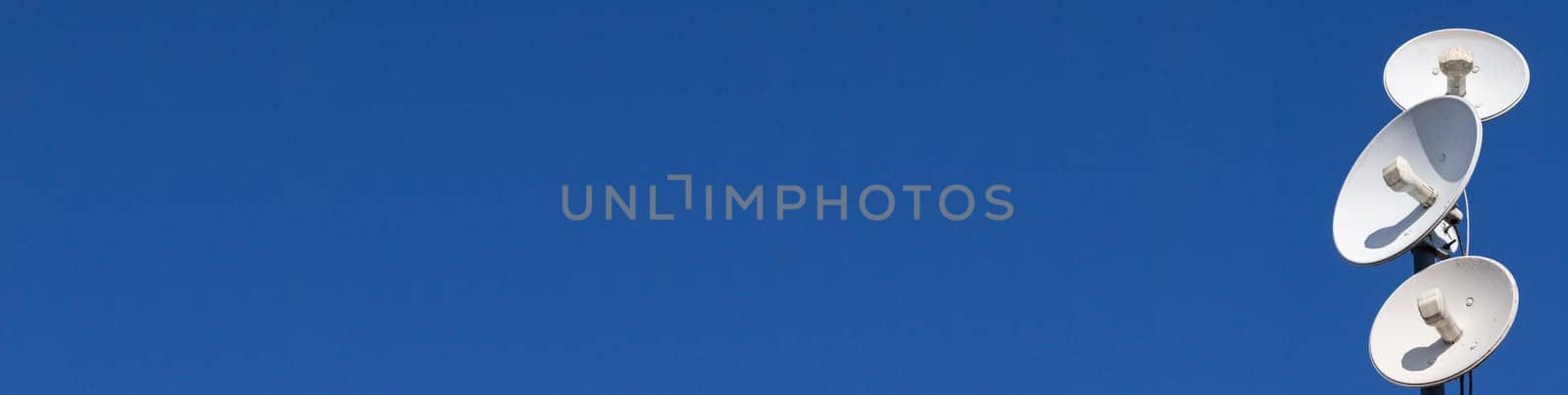 White telecommunications antennas on a single mast high above the city against the background of a blue sky. Technology of digital sending and receiving of data packets. Panoramic view.