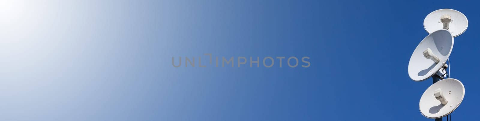 White telecommunications antennas on a single mast high above the city against the background of a blue sky. Technology of digital sending and receiving of data packets. Panoramic view. Blue background.