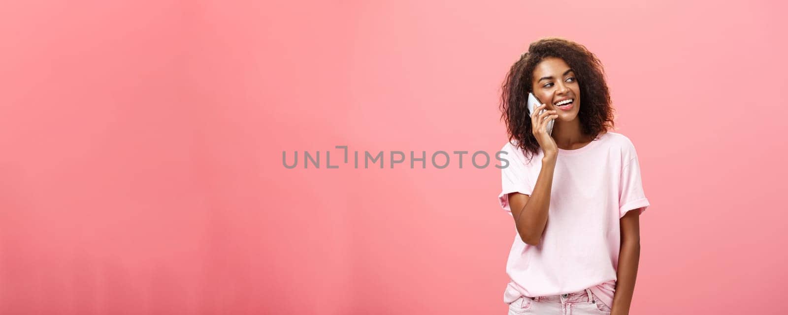 Woman calling boyfriend come pick her up after practice standing on street carefree and chill gazing right with broad satisfied smile holding smartphone near ear posing over pink background by Benzoix