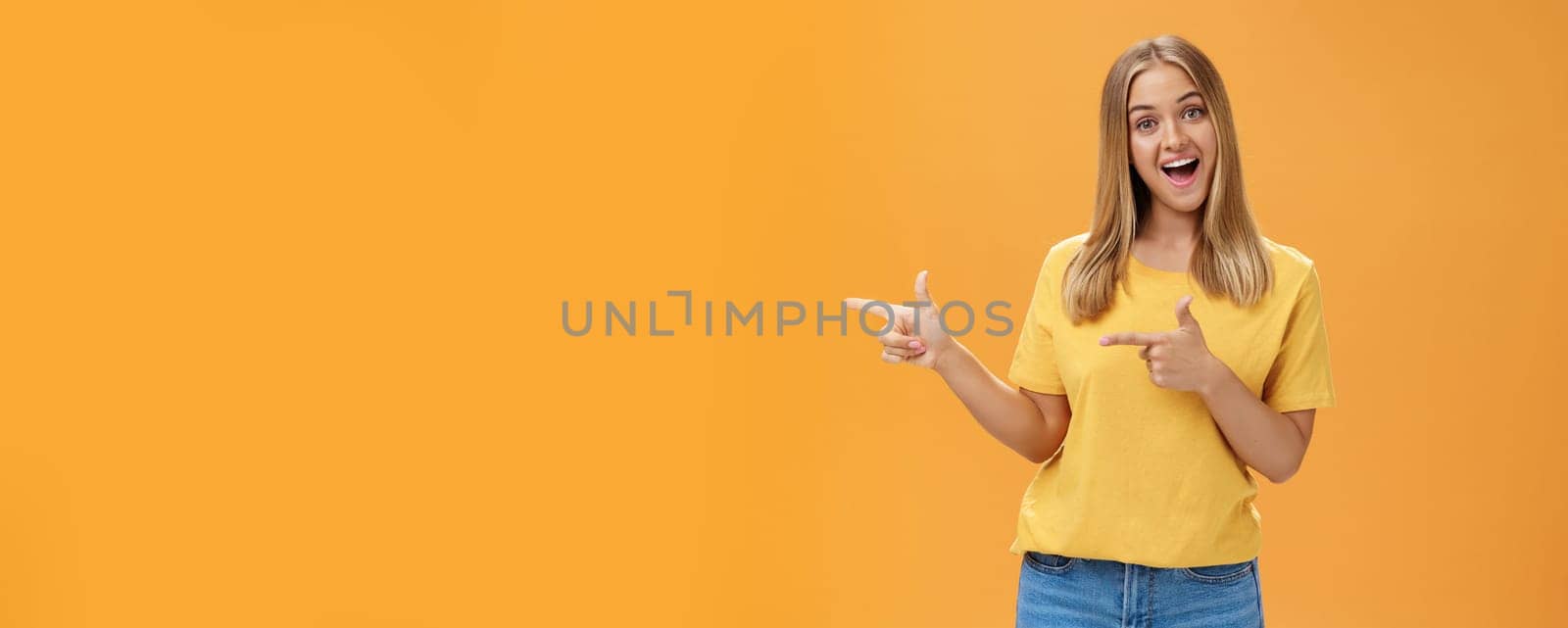 Check out copy sapce of dream. Upbeat good-looking pleasant female shop assistant in t-shirt pointing left with finger guns and smiling amused at camera recommending to watch that direction. Advertisement concept