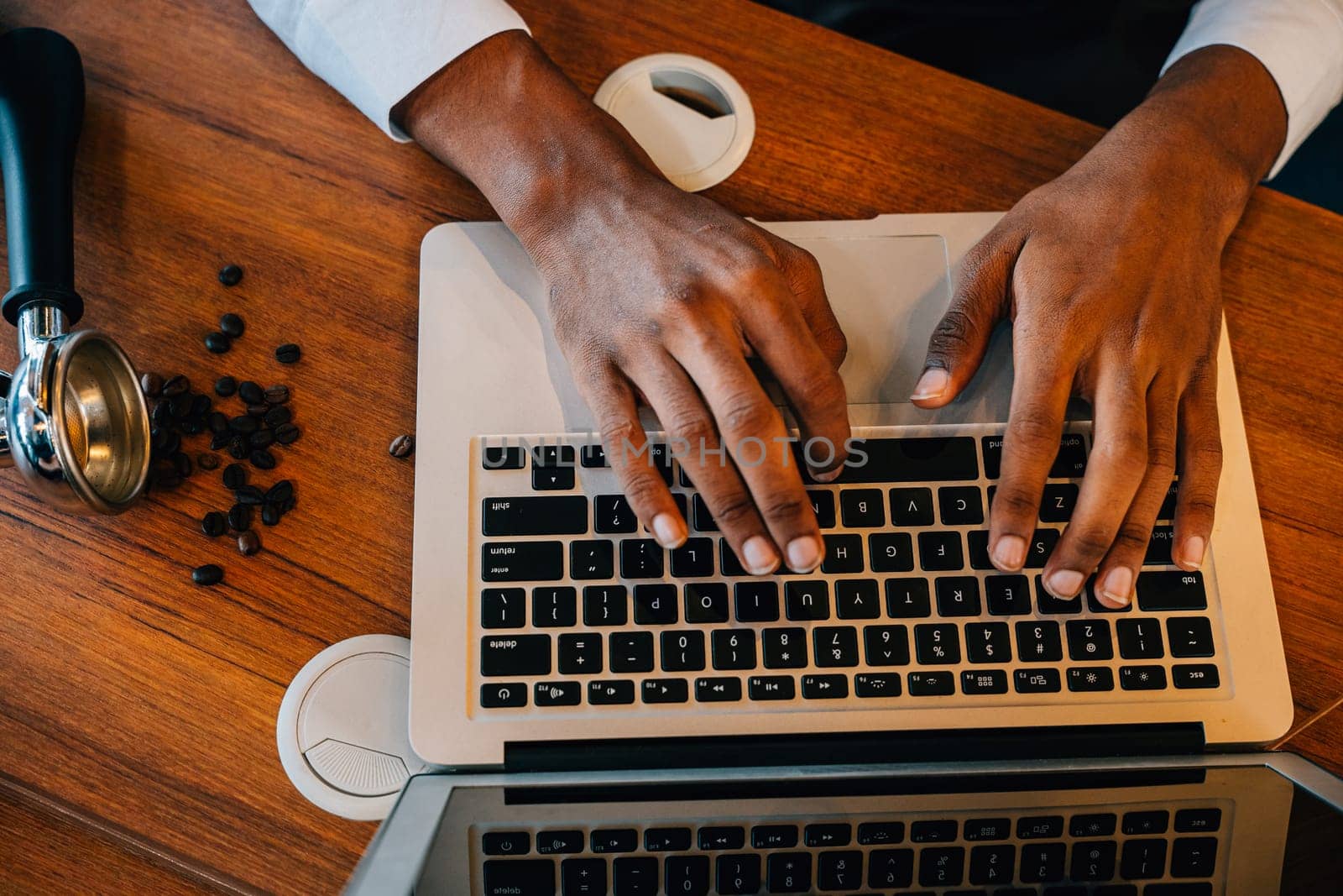 In the modern roastery office a multitasking business owner also a barista checks bean quality on laptop and machinery. Quality check assures premium coffee beans. Precision is the norm.