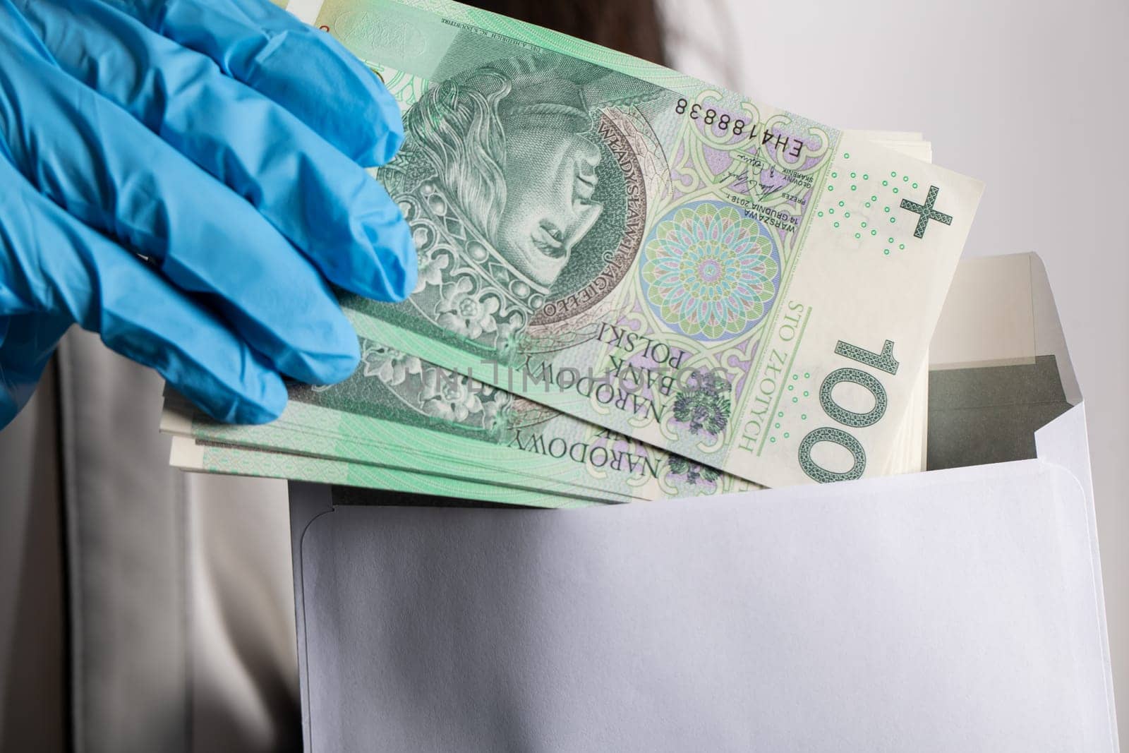 The woman slips a bundle of one hundred Polish zloty banknotes into a white envelope.