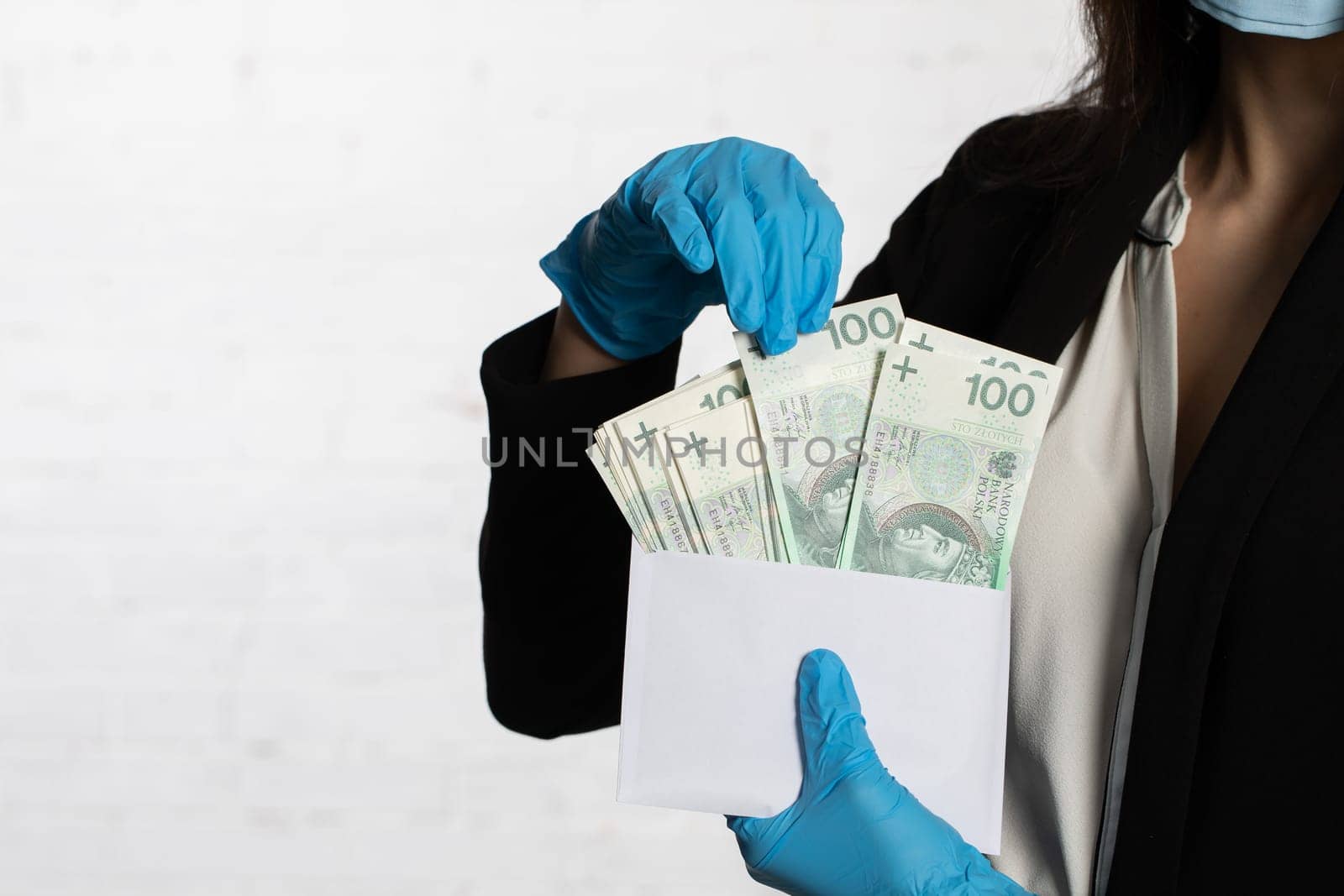 The woman slips a bundle of one hundred Polish zloty banknotes into a white envelope.