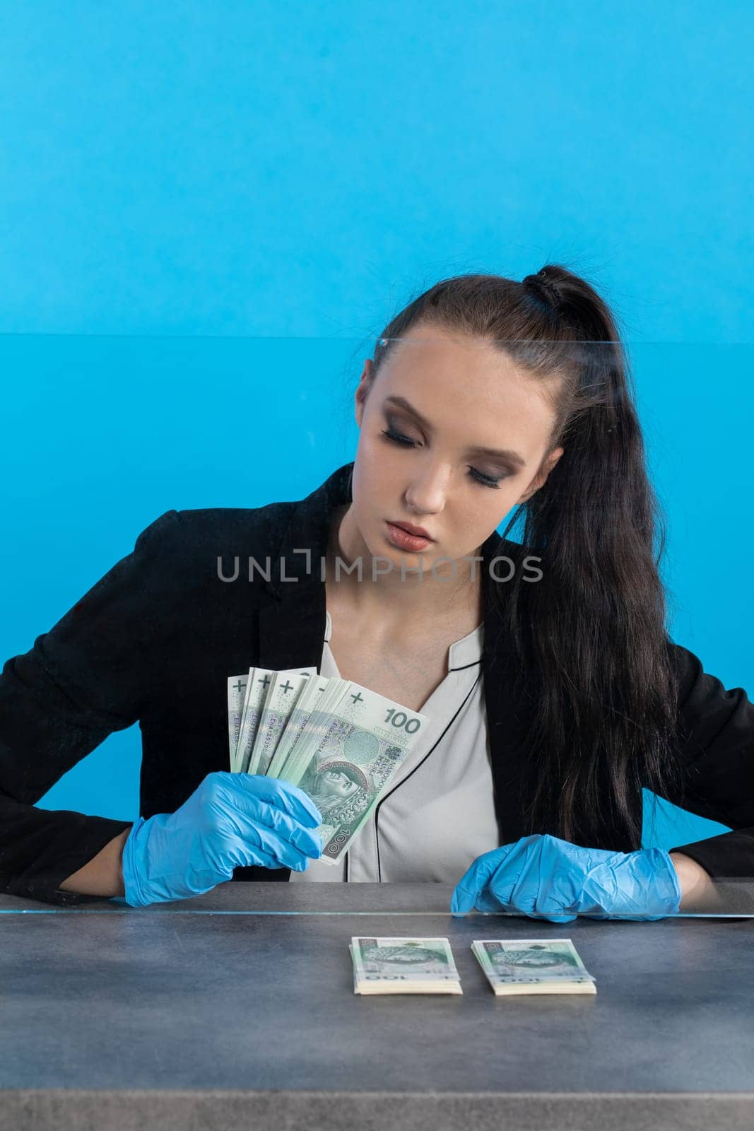 Hand counting banknotes by a young woman at the cashier's window in a large banking branch.